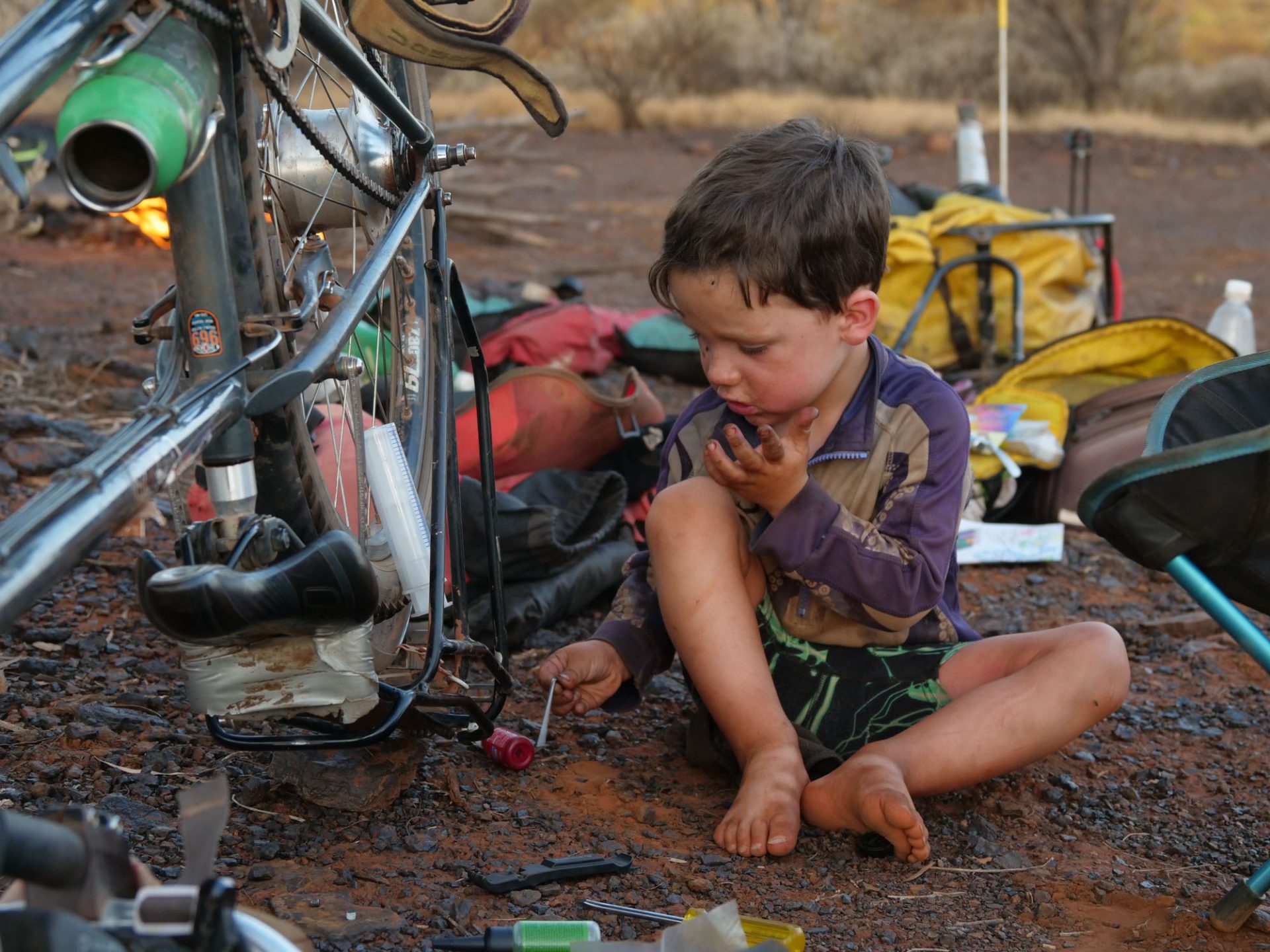 A barefoot Wilfy plays in the dirt next to an upturned bike.