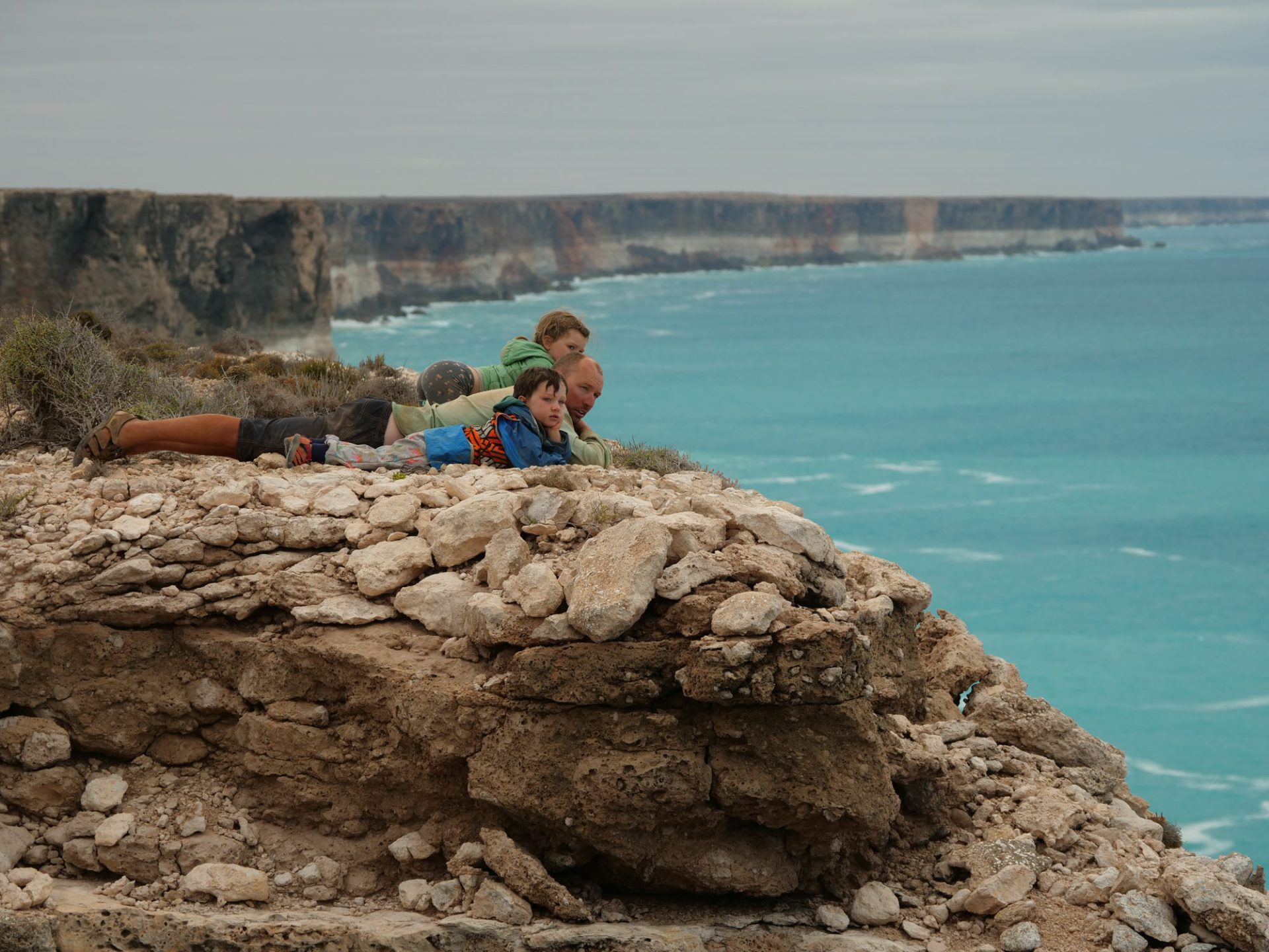 Andrew and both children lie on a cliff, looking over a pristine blue sea. 
