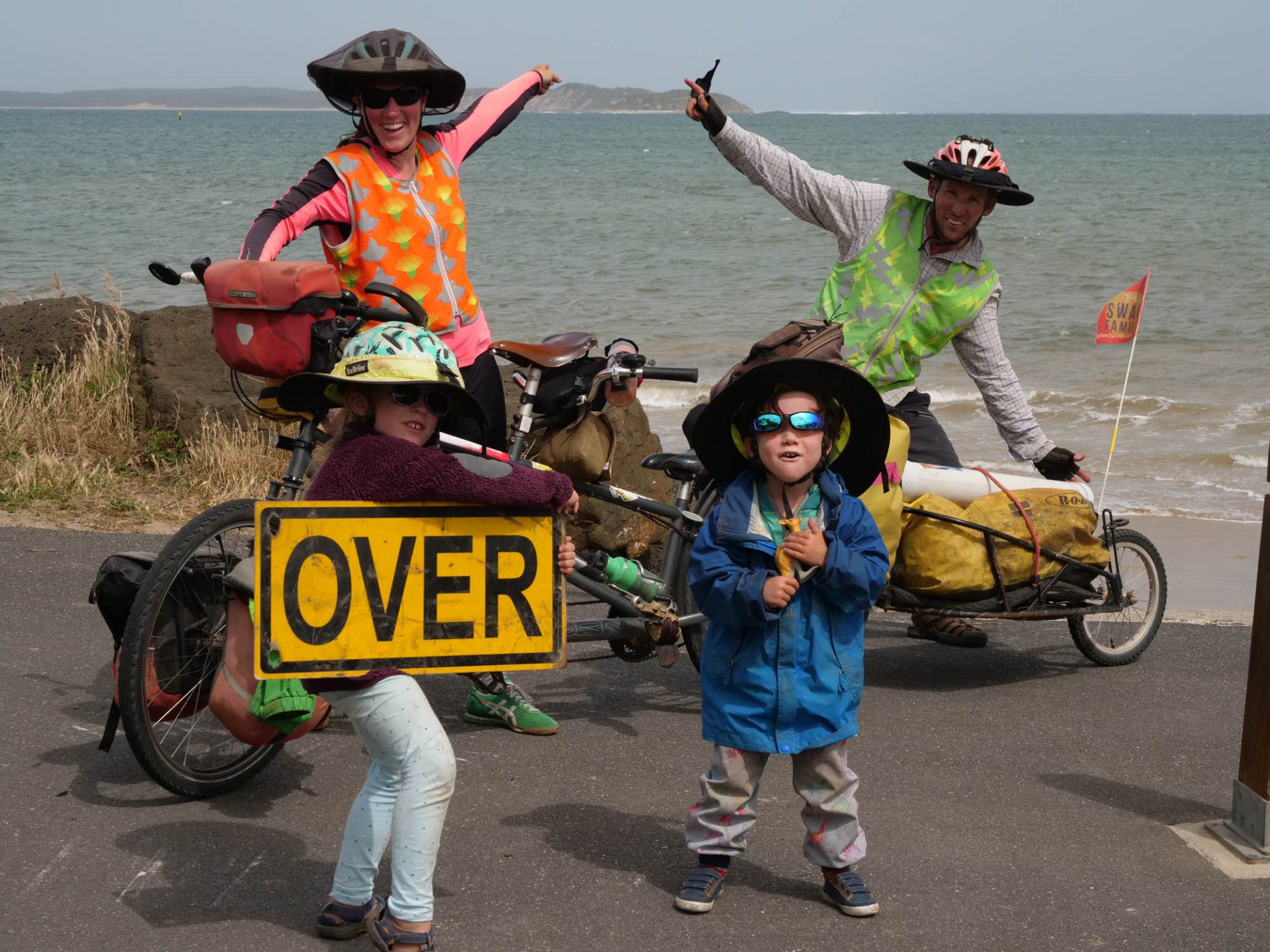 The family poses, presumably near the end of their journey, with Hope holding a sign that says 'OVER'. 