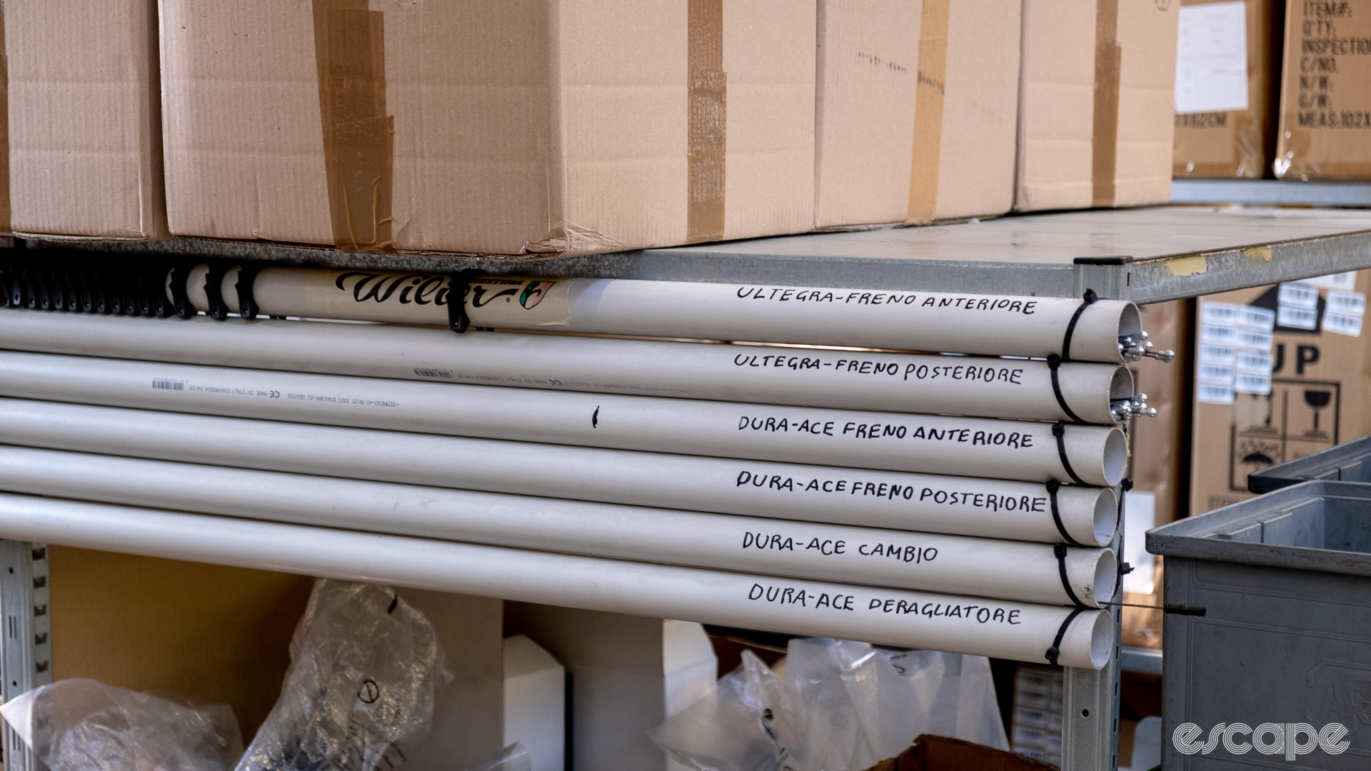 The image shows some long white pipes storing brake and mechanical shift cables with the Dura-Ace and Ultegra names written on some of the pipes.  