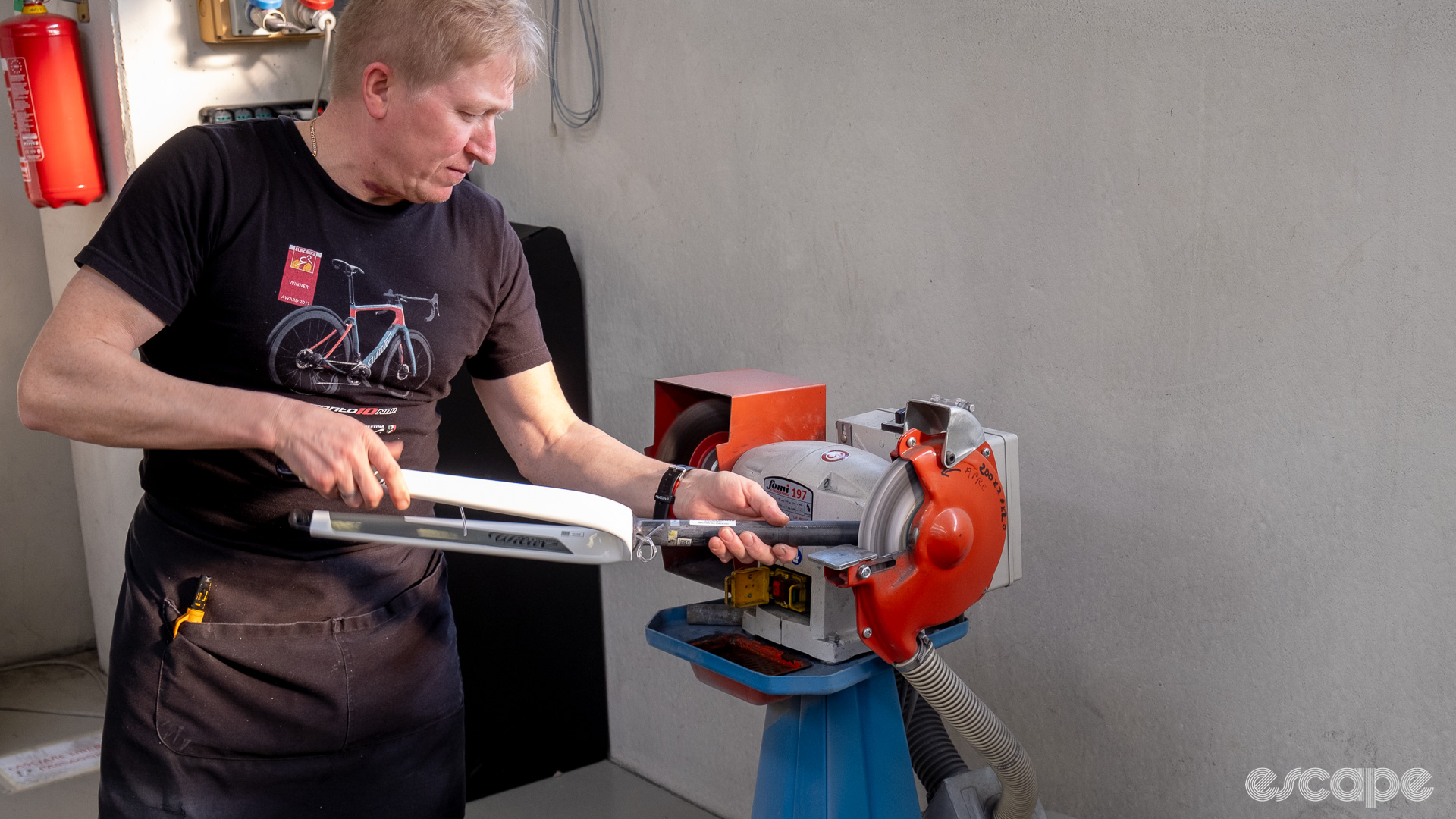 The photo shows a mechanic sanding a steerer tube on a bench grinder. 