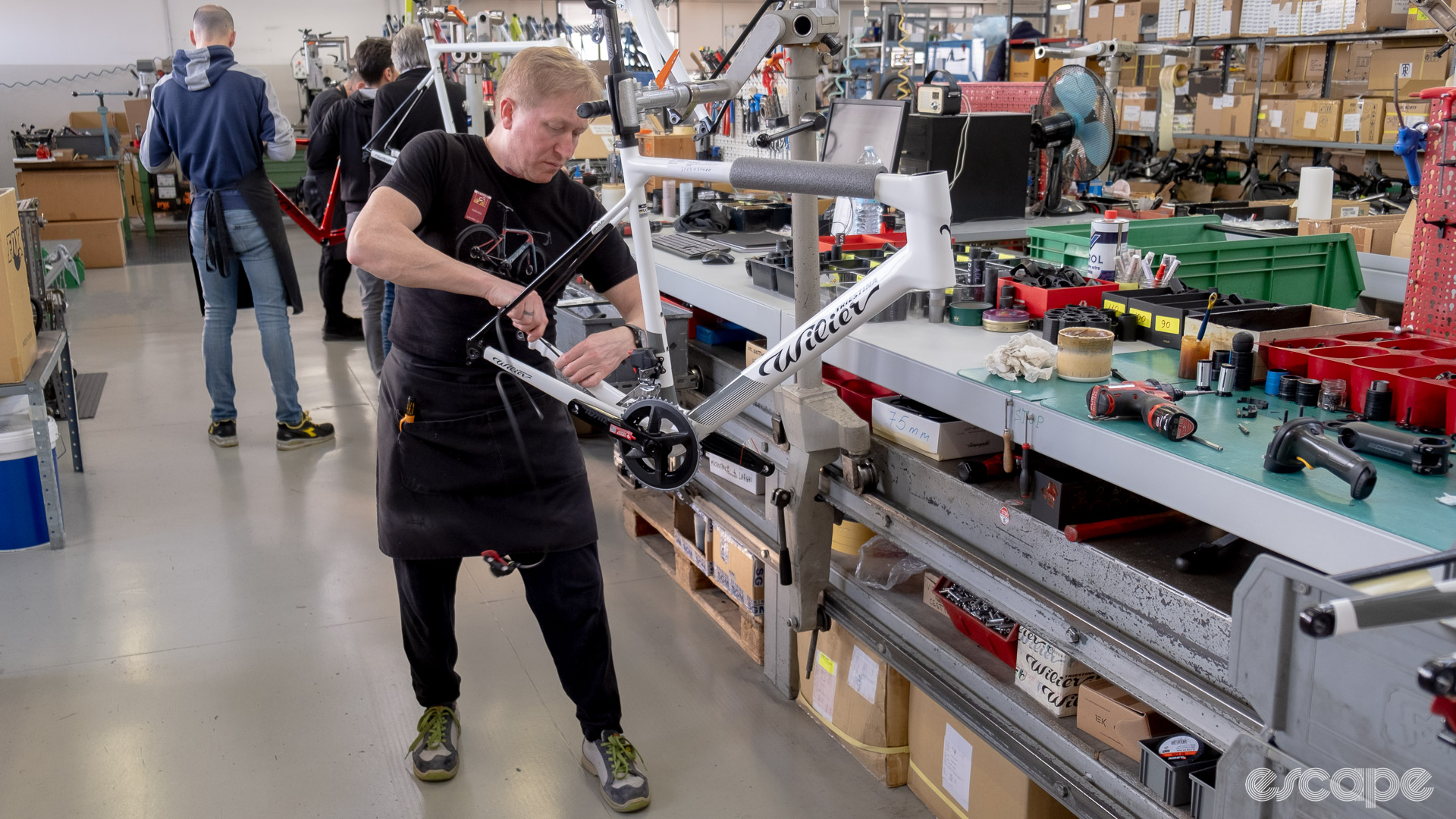 The photo shows a mechanic routing a rear brake hose through a frame on Wilier's assembly line.