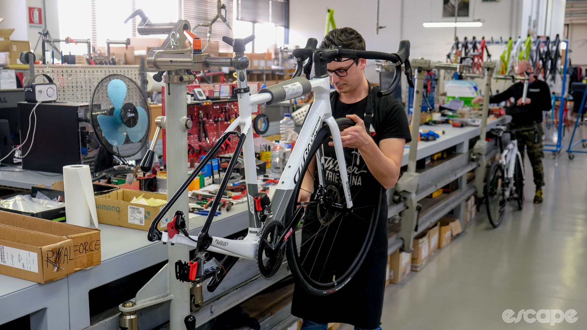 The photo shows a mechanic inserting a front wheel on a bike. 