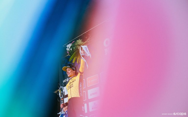 A shot of MARIANNE VOS framed by flags on the podium of Omloop Het Nieuwsblad