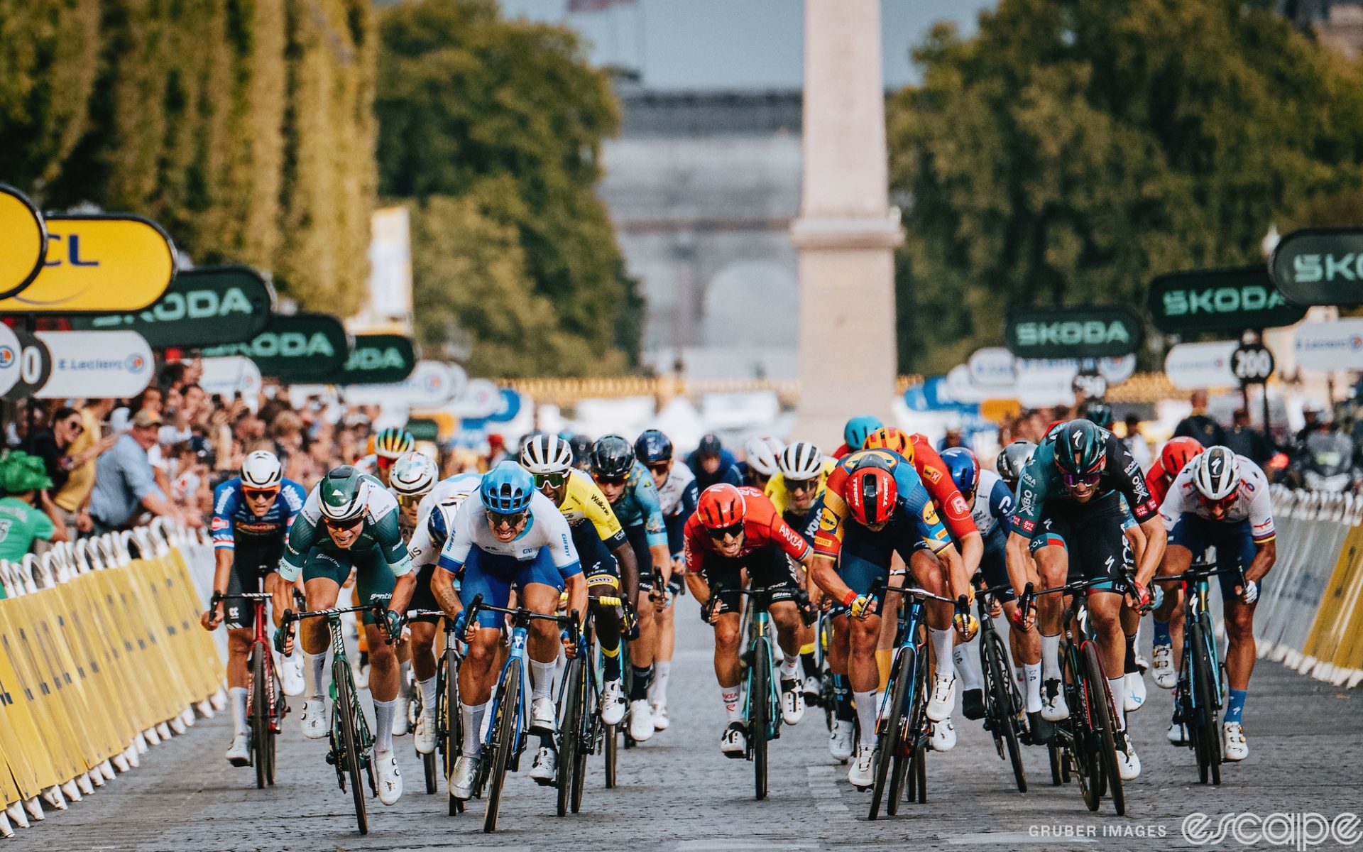 The final sprint on the Champs in 2023. Riders lean their bikes as they make a mad dash for the line. Some look forward while others have their heads bent low.