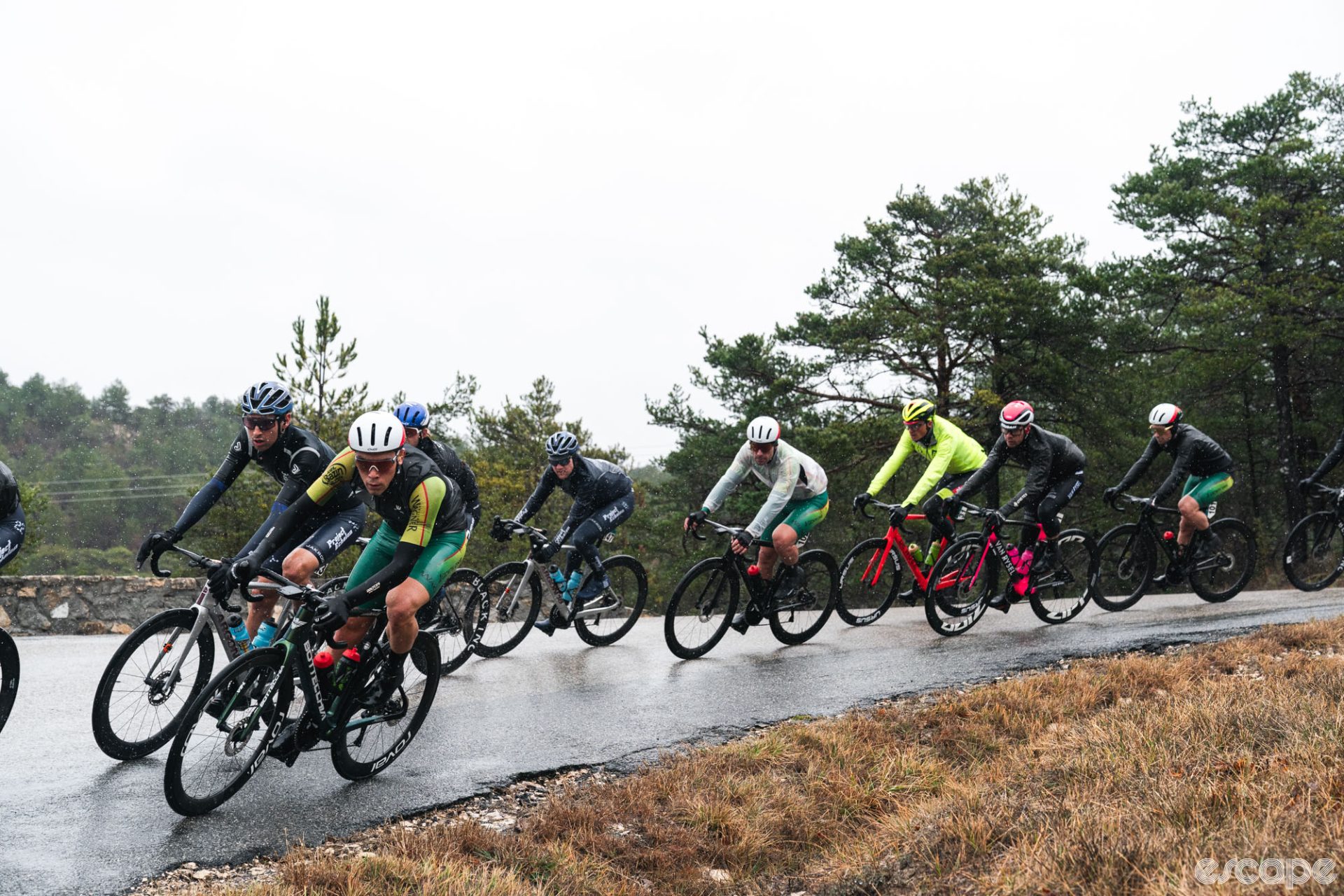Riders carefully navigate a corner on a descent in Tour de la Provence. The road is wet, the sky a flat gray, and everyone looks cold and unhappy.