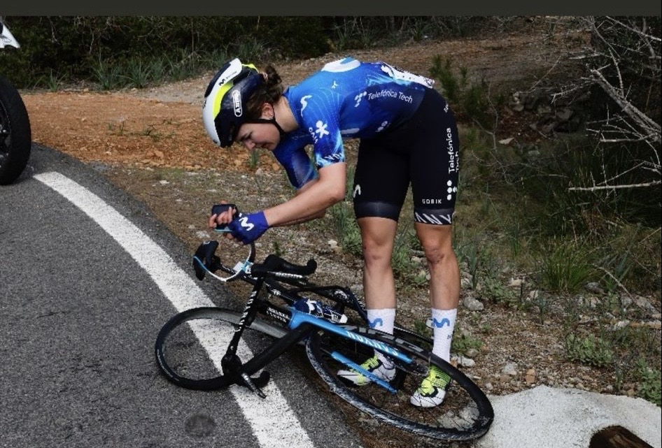 The photo shows a Movistar rider attending to their bike on the ground with the front tyre clearly dismounted from the front rim.