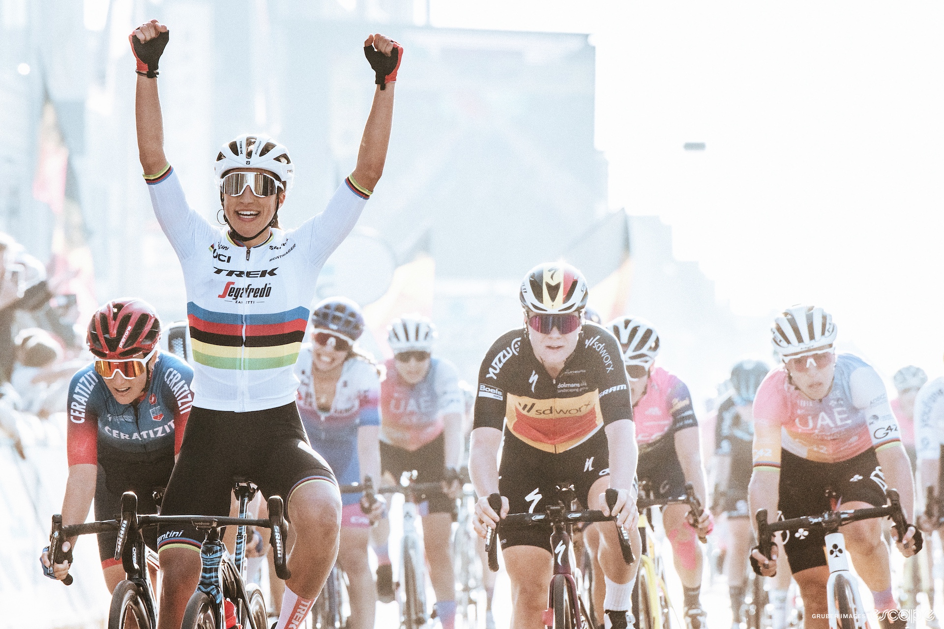 Elisa Balsamo celebrates as she wins 2022 Gent-Wevelgem. She has her arms in the air as riders including Lotte Kopecky sit up behind her in frustration.