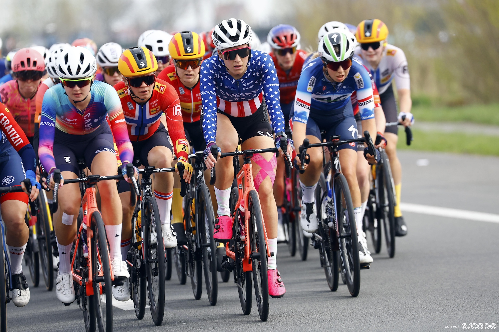 A group of women race bikes. Chloe Dygert is on the front in her red white and blue national champion jersey.