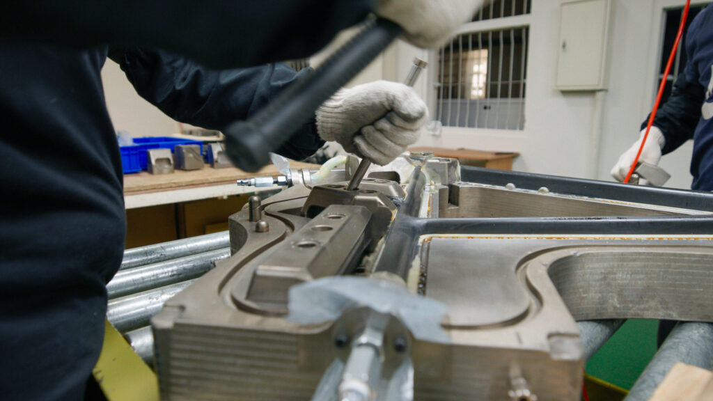 A Factor employee uses a mallet and chisel to pry a mould insert out of the larger clamshell mould. In the mould sits a frame that has just been cured.