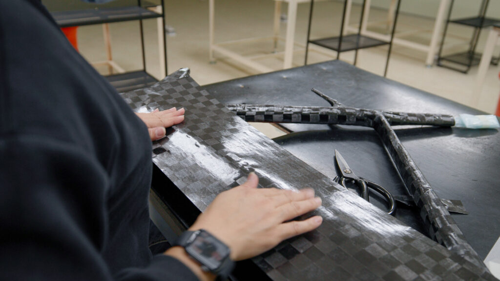 The image shows an operative laying carbon fibre onto a frame during production. 