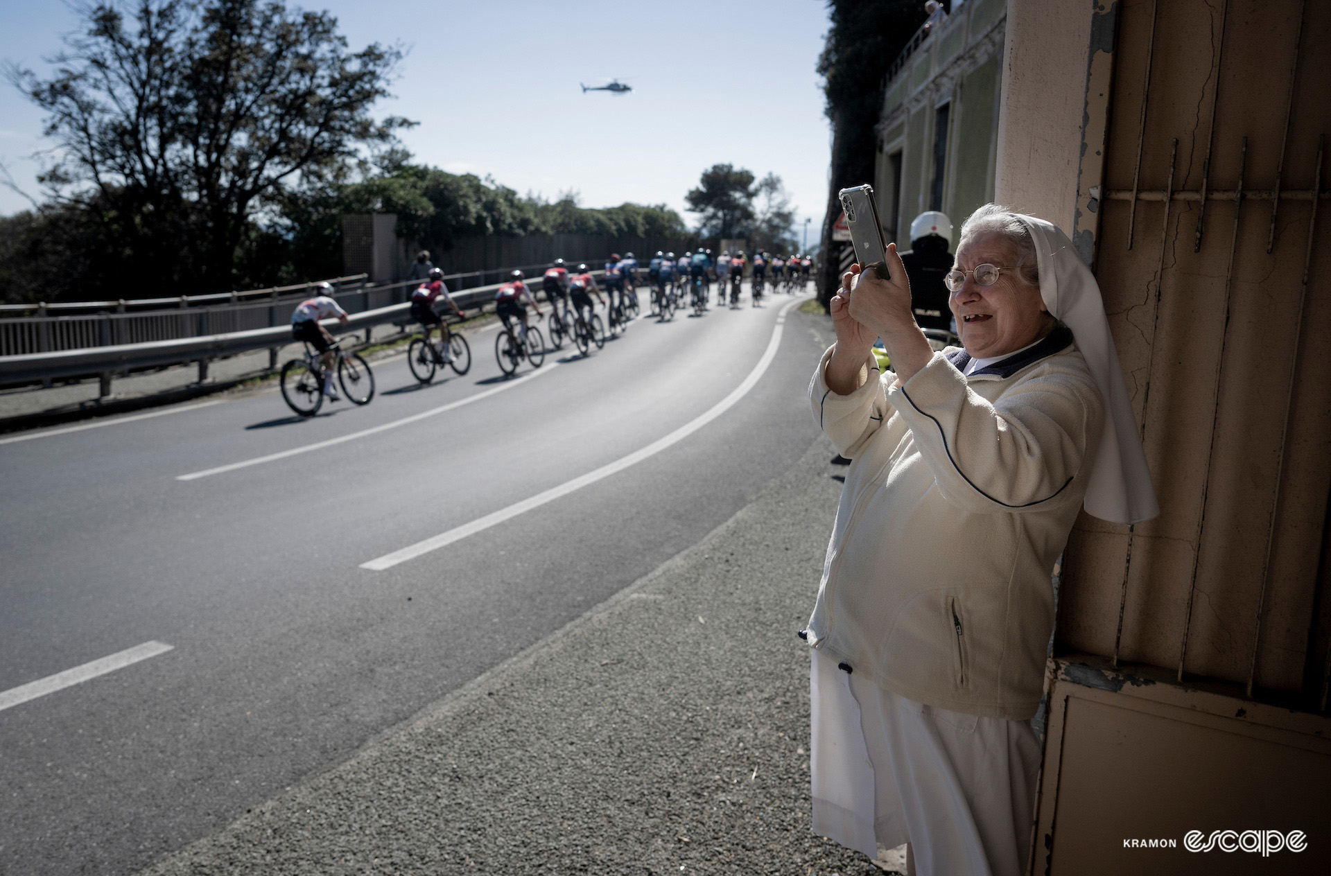 A nun holds her phone aloft as the peloton passes her convent during Milan-San Remo 2024.