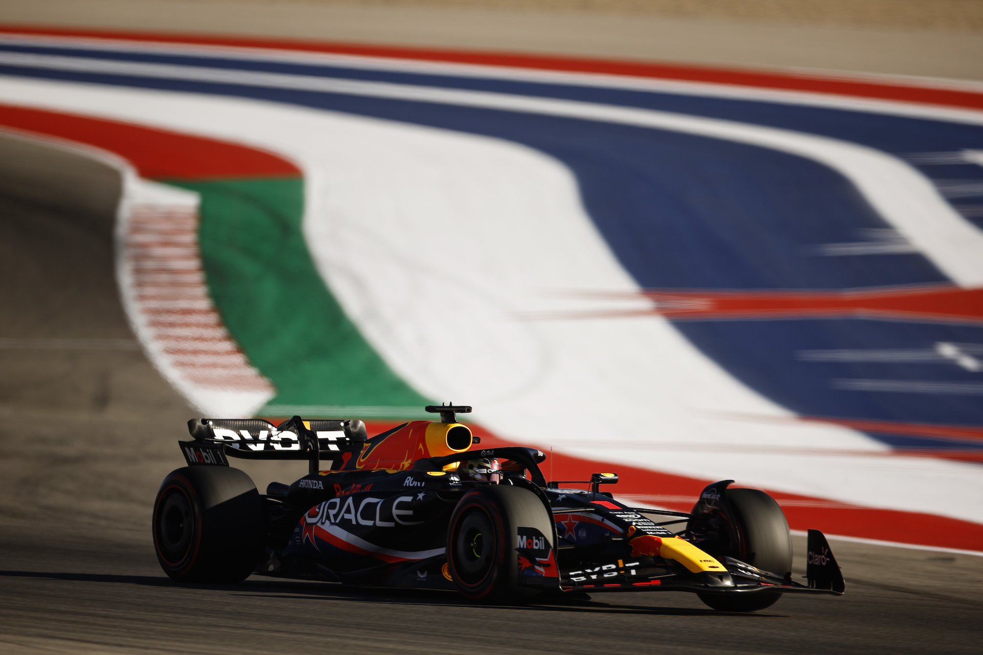 Max Verstappen drives on the Circuit of the Americas in the F1 Grand Prix in Austin, Texas. He's alone, and behind him a red-white-and-blue paint job stretches in ribbons on the apron of the raceway. America.