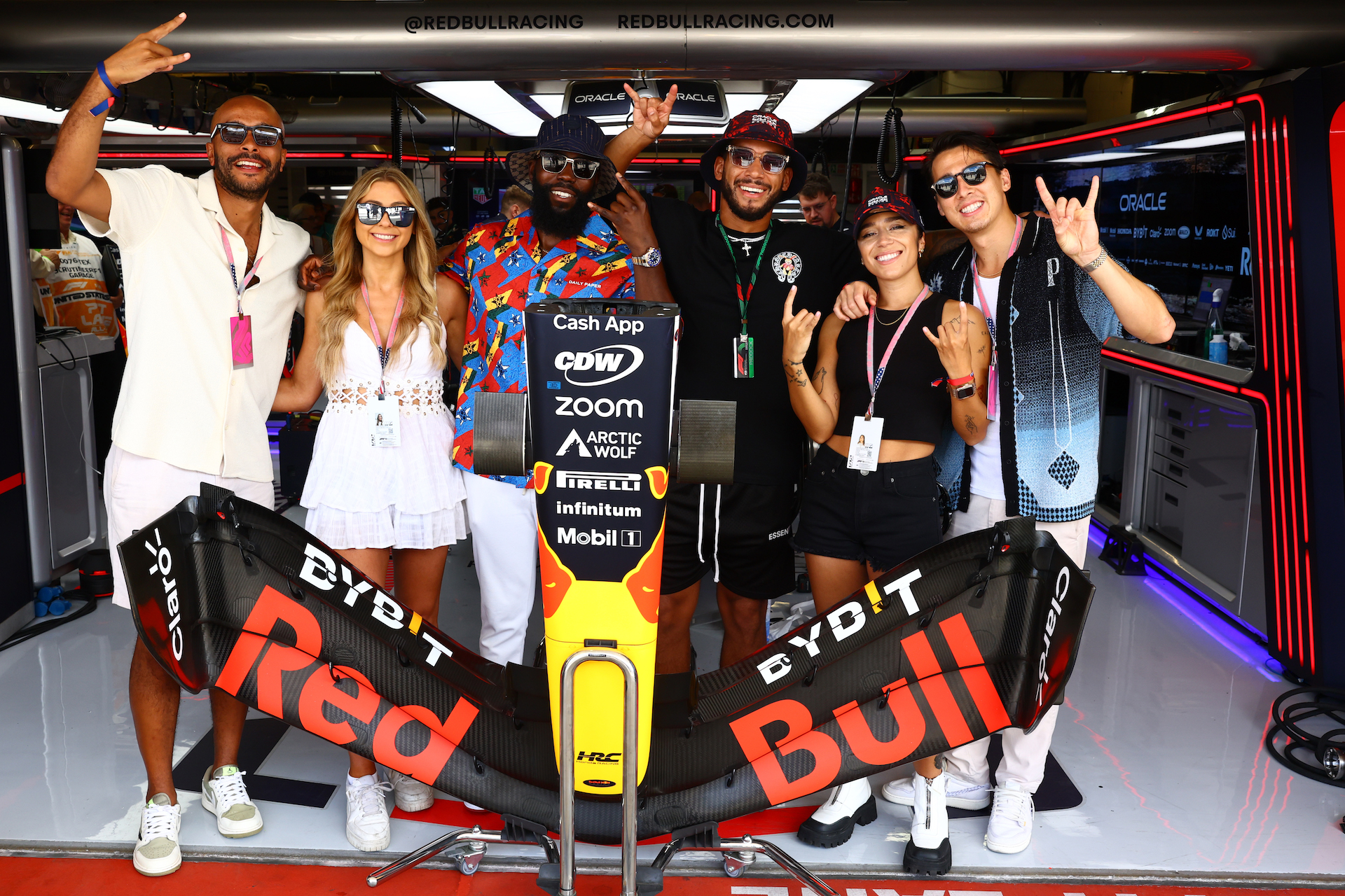 From left to right, Stefan Xavier, Kate Ovens, David Alorka, Josh Denzel, Chelcee Grimes, Michael Timbs pose for a photo in the Red Bull Racing garage prior to the F1 Grand Prix of United States at Circuit of The Americas on October 22, 2023 in Austin, Texas. They are smiling and most are doing the "hook 'em horns" hand gesture.