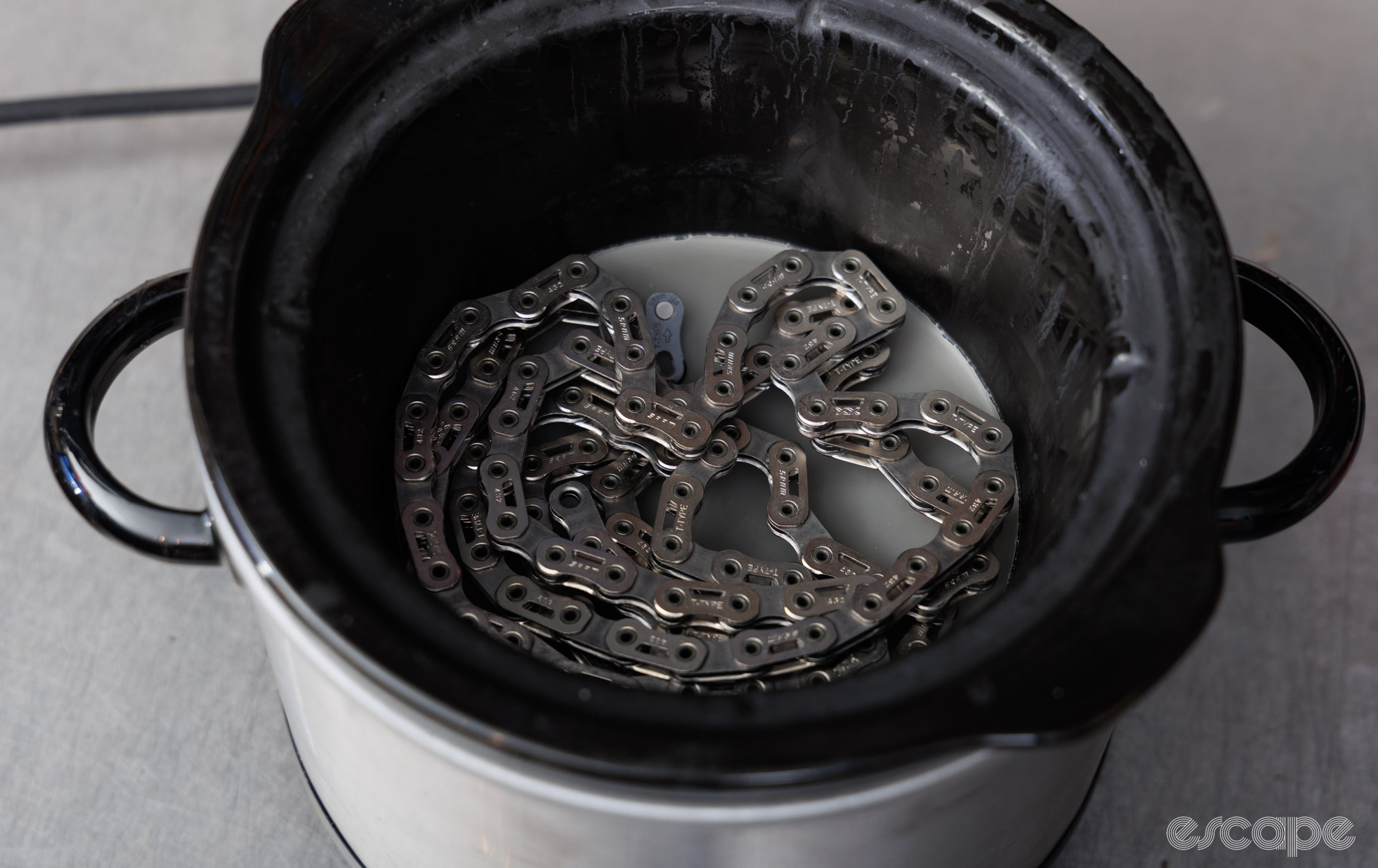 A SRAM chain sits in a slow cooker with wax. 