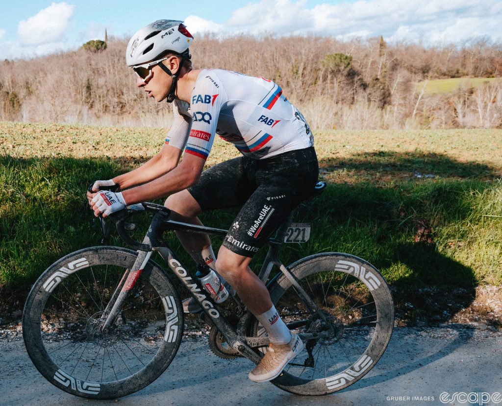 Tadej Pogačar on race day at Strade Bianche. The helmet is swapped for an aero version, the wind-dragging knee and arm warmers are gone, and the jersey and shorts are now a skinsuit.
