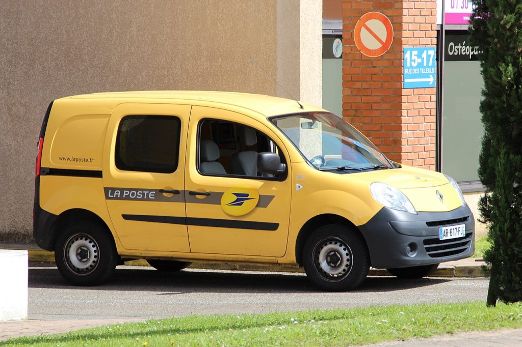 A bright yellow La Poste Renault Kangoo van sitting on the street. 