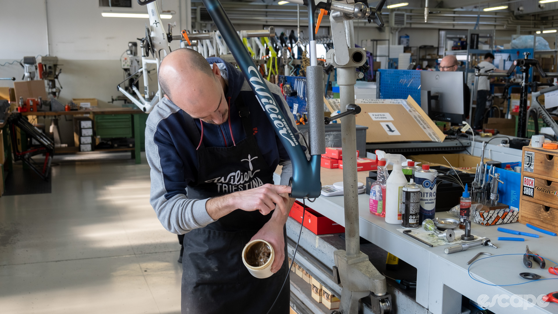 The photo shows a mechanic adding grease to a frame in preparation for adding the headset bearing.