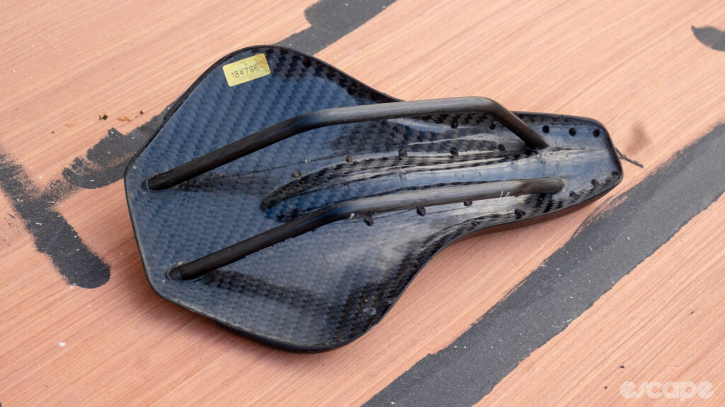The image shows the underside of the carbon shell on a Wove Mags carbon fibre bike saddle.