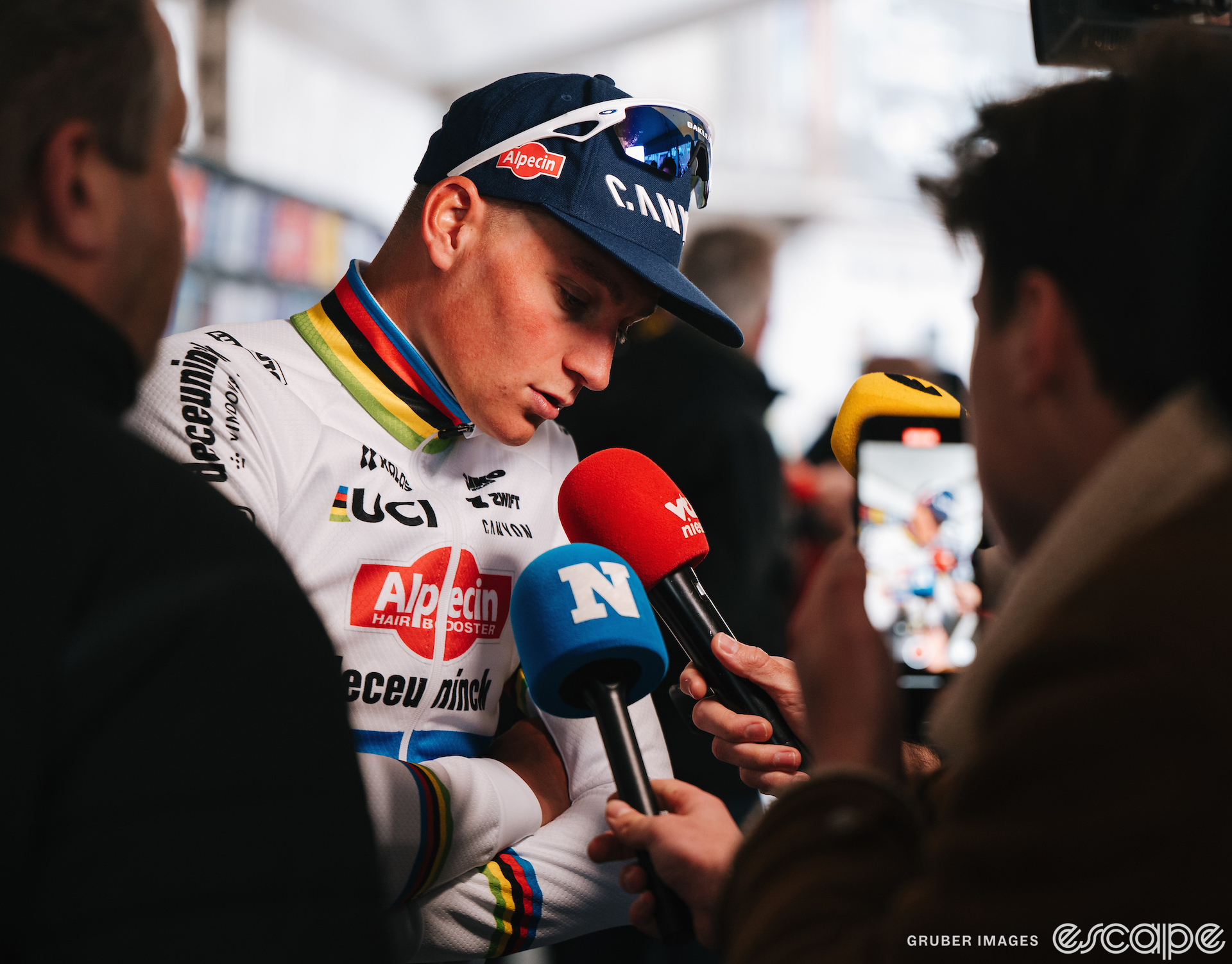 Mathieu van der Poel bows his head slightly as he speaks into two proferred reporters' microphones. He has a look of concentration and his eyes are slightly downcast.