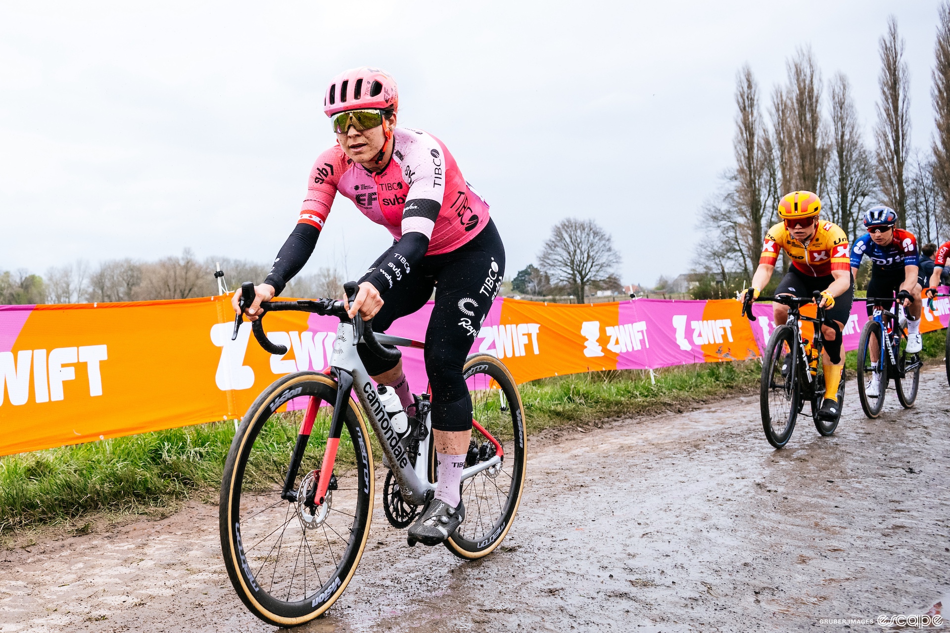 Alison Jackson leads on some wet, muddy cobbles at the 2023 Paris-Roubaix Femmes. She has a slight gap over the riders behind.