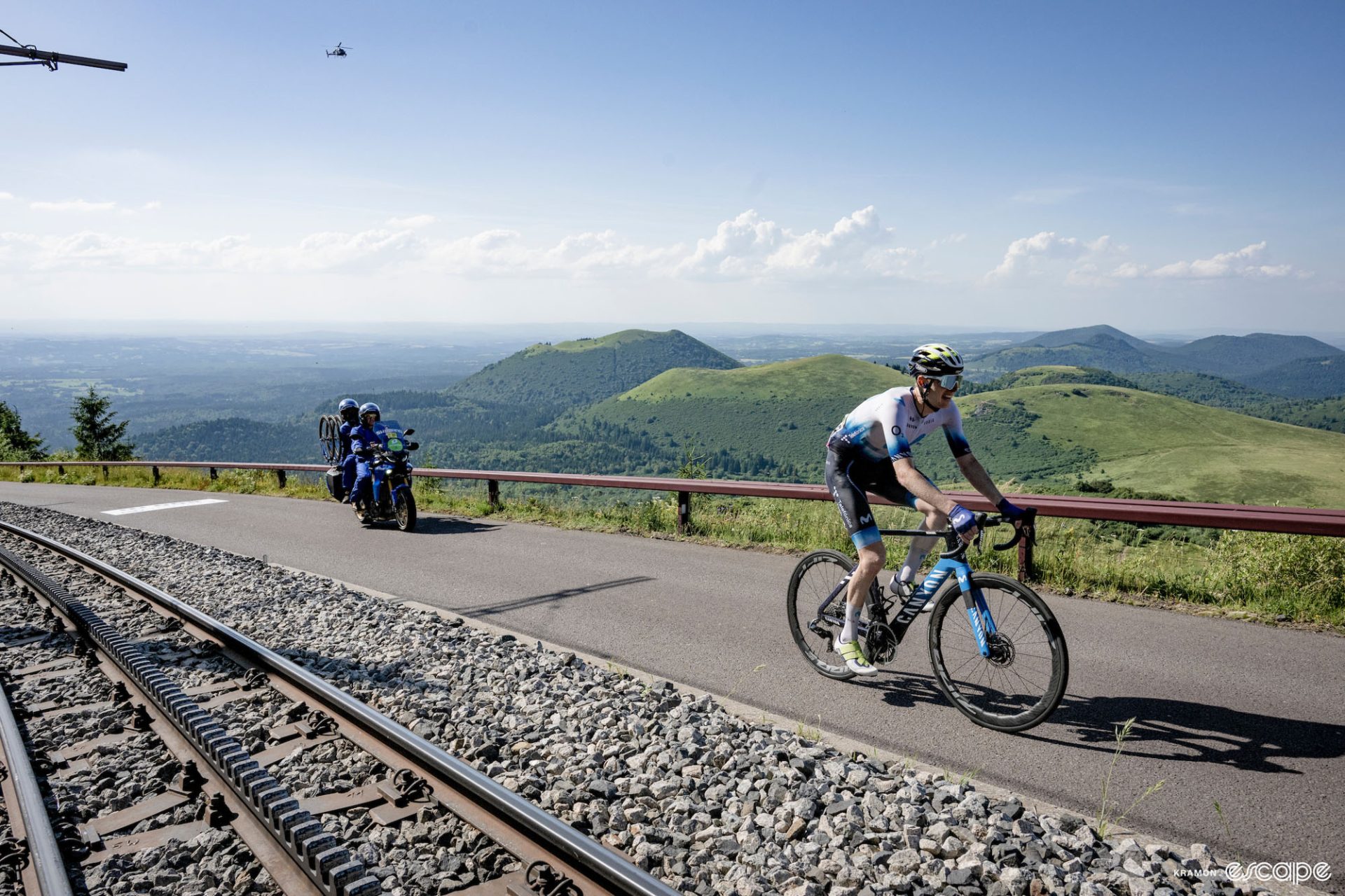 Matteo Jorgenson climbs the Puy de Dome in the solo breakaway at the 2024 Tour de France. Because the climb was closed to fans, he's all alone, with just a follow motorbike with spare wheels. Above and behind him, a helicopter looms, and he rides alongside the cog railway, a reminder of how steep the climb is.