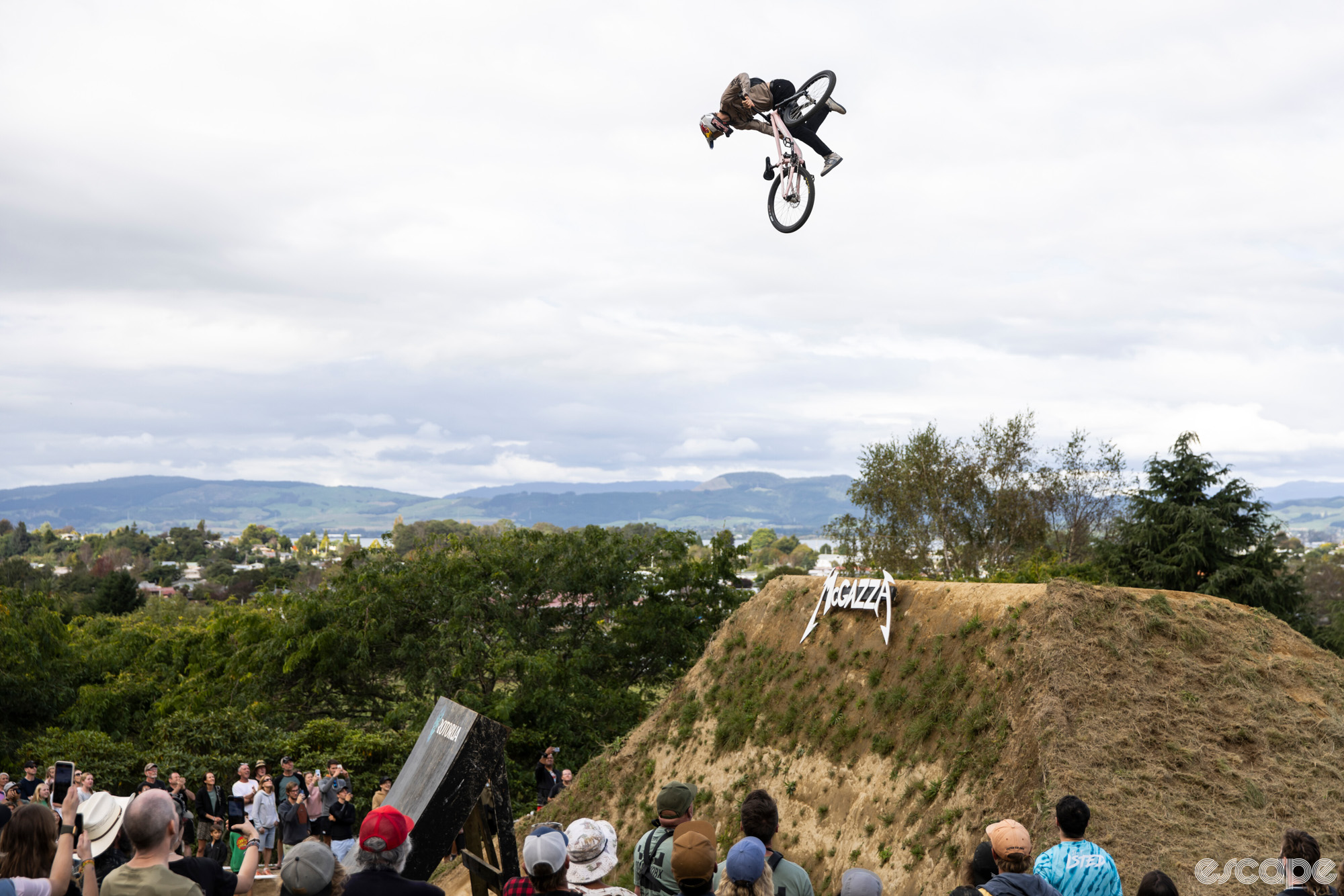 Emil Johannson launches a trick off a ramp at Crankworx Rotorua. He's about 20 feet in the air, and has whipped the bike through at least a 360-degree spin and is looking down as he prepares to catch the pedals again before landing.