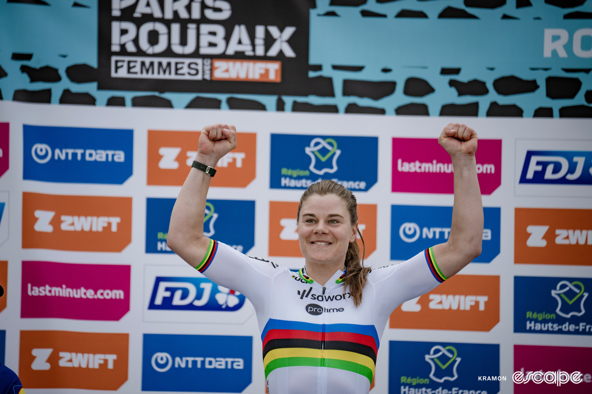 A woman raises her arms in triumph on the podium of a bike race