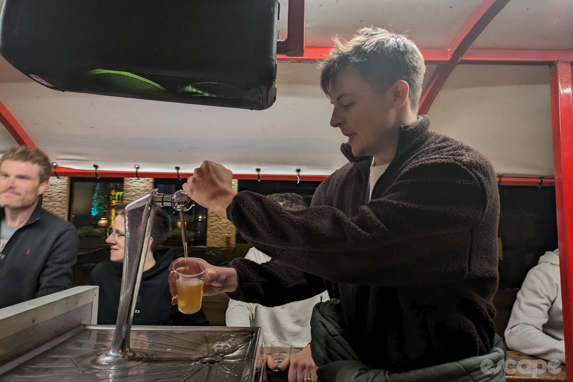 Jonny pouring beers into little plastic cups, with a very serious expression.