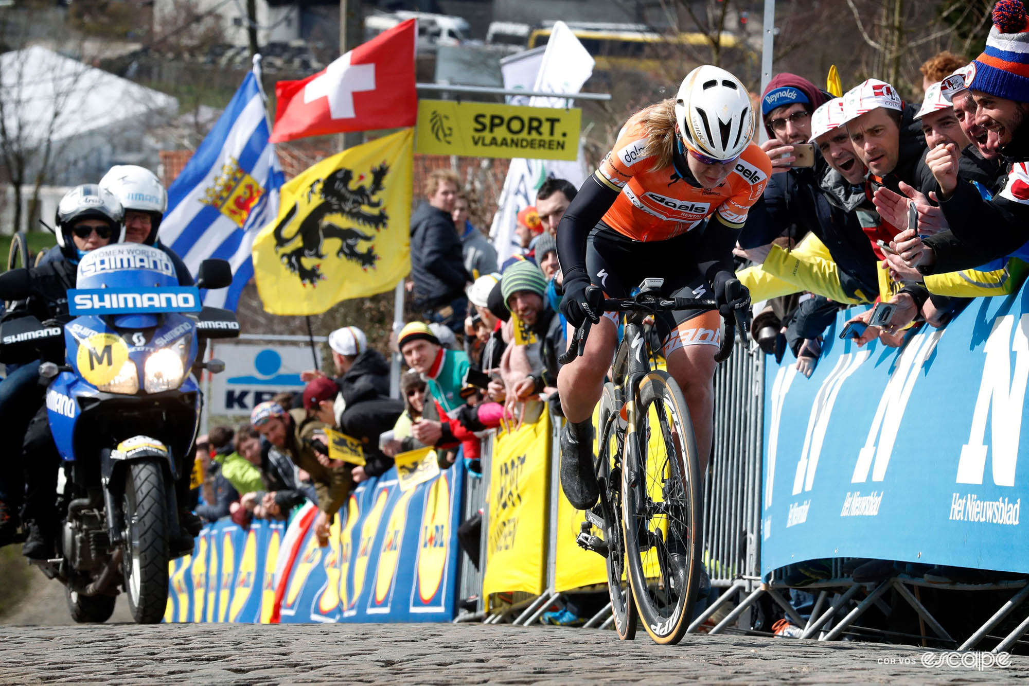 Anna van der Breggen climbs solo on the Paterberg. Her head is down as she focuses on the task, and behind onl a Shimano neutral support moto and fans lining the barriers are seen; there are no other competitors in the picture.