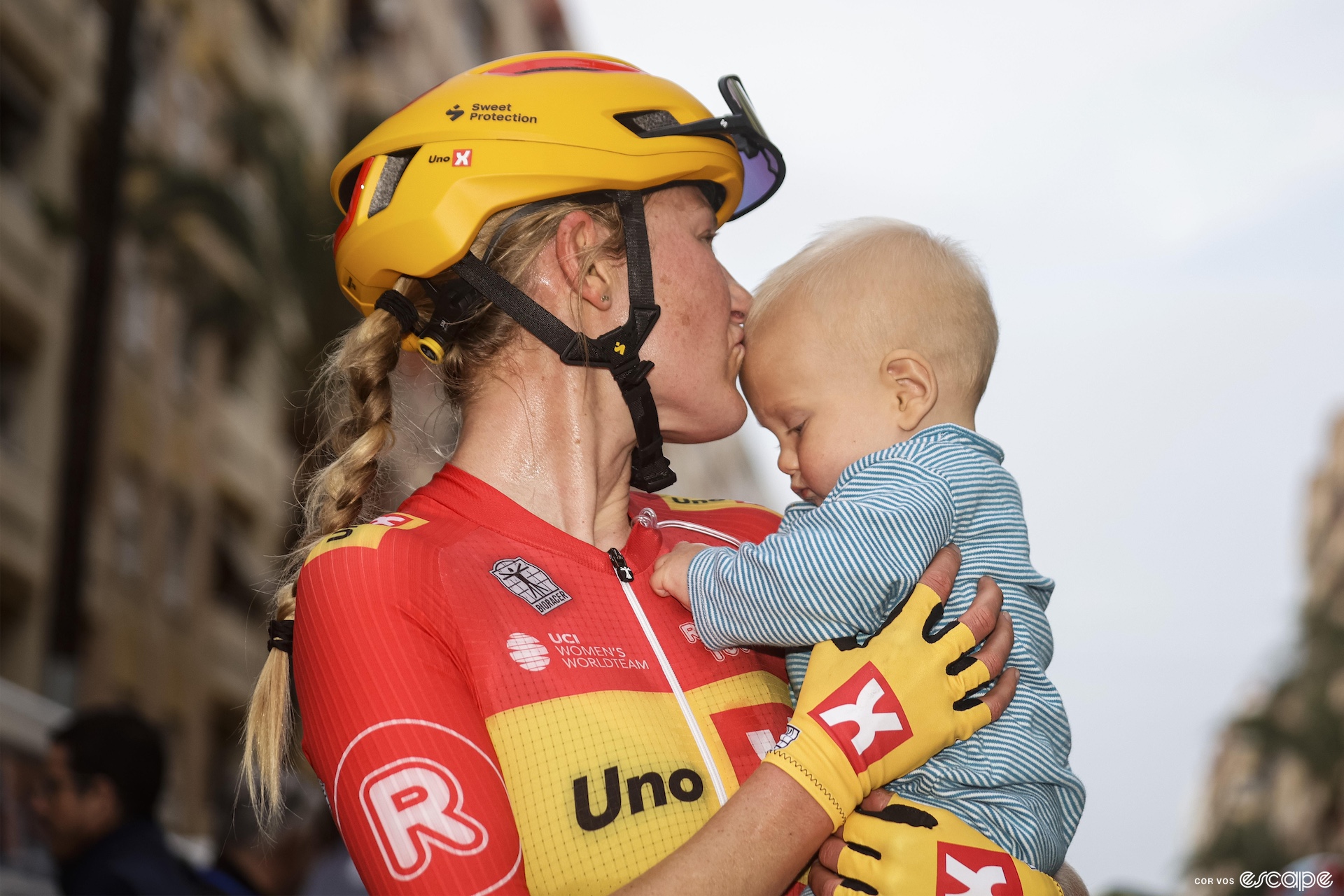 A woman in cycling kit gives her son a kiss on the forehead before starting a bike race