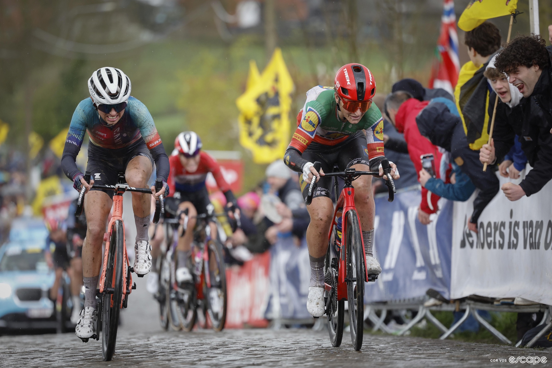 Two women race bikes over cobbled roads