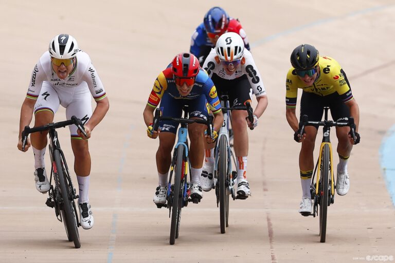 Four women sprint for the finish line of a bike race in a Velodrome.