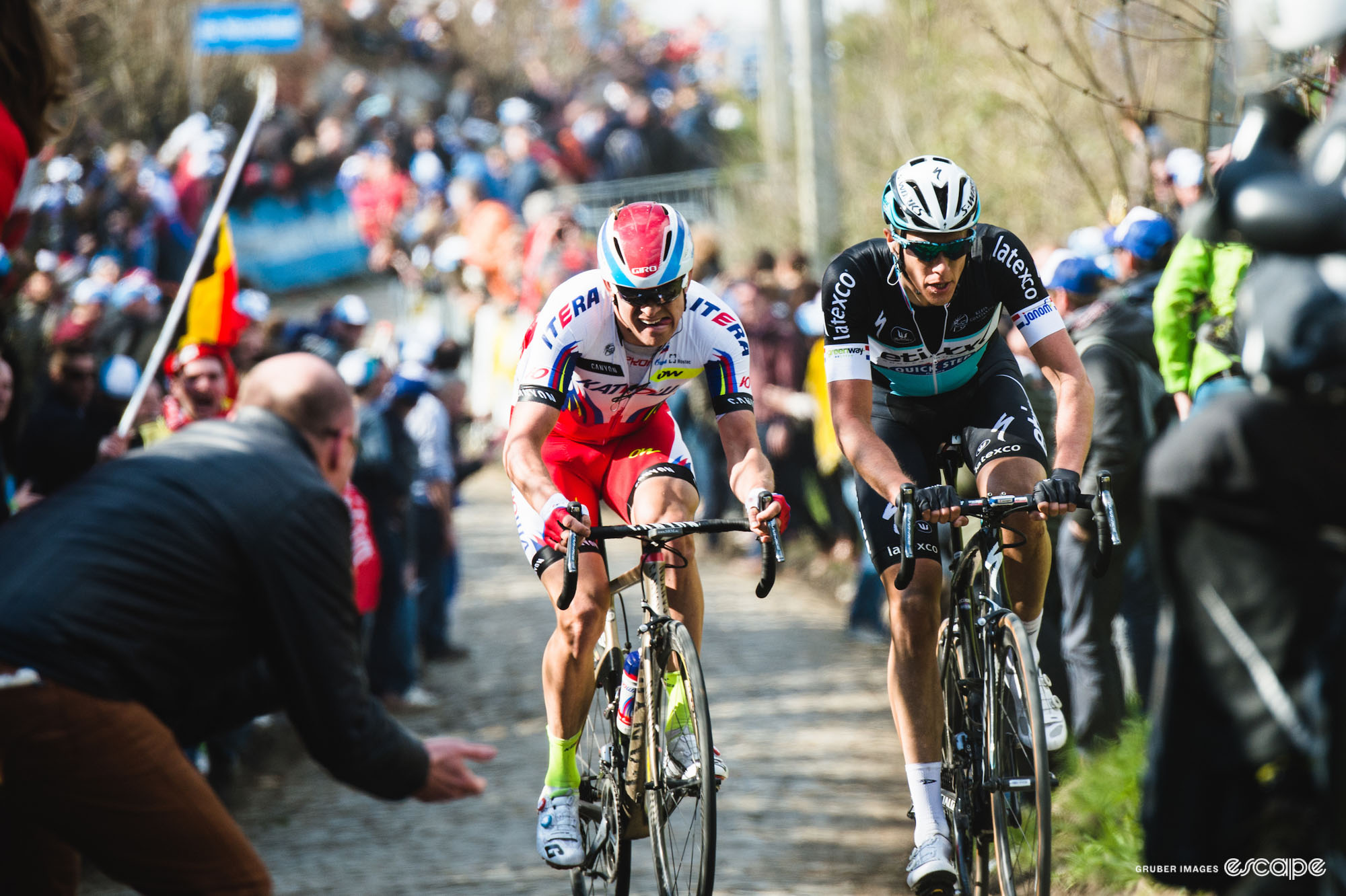 Alexander Kristoff and Niki Terpstra ride on cobbles at the Tour of Flanders in 2015. Terpstra leads, looking smooth and almost impassive, while Kristoff is grimacing as he holds the wheel.