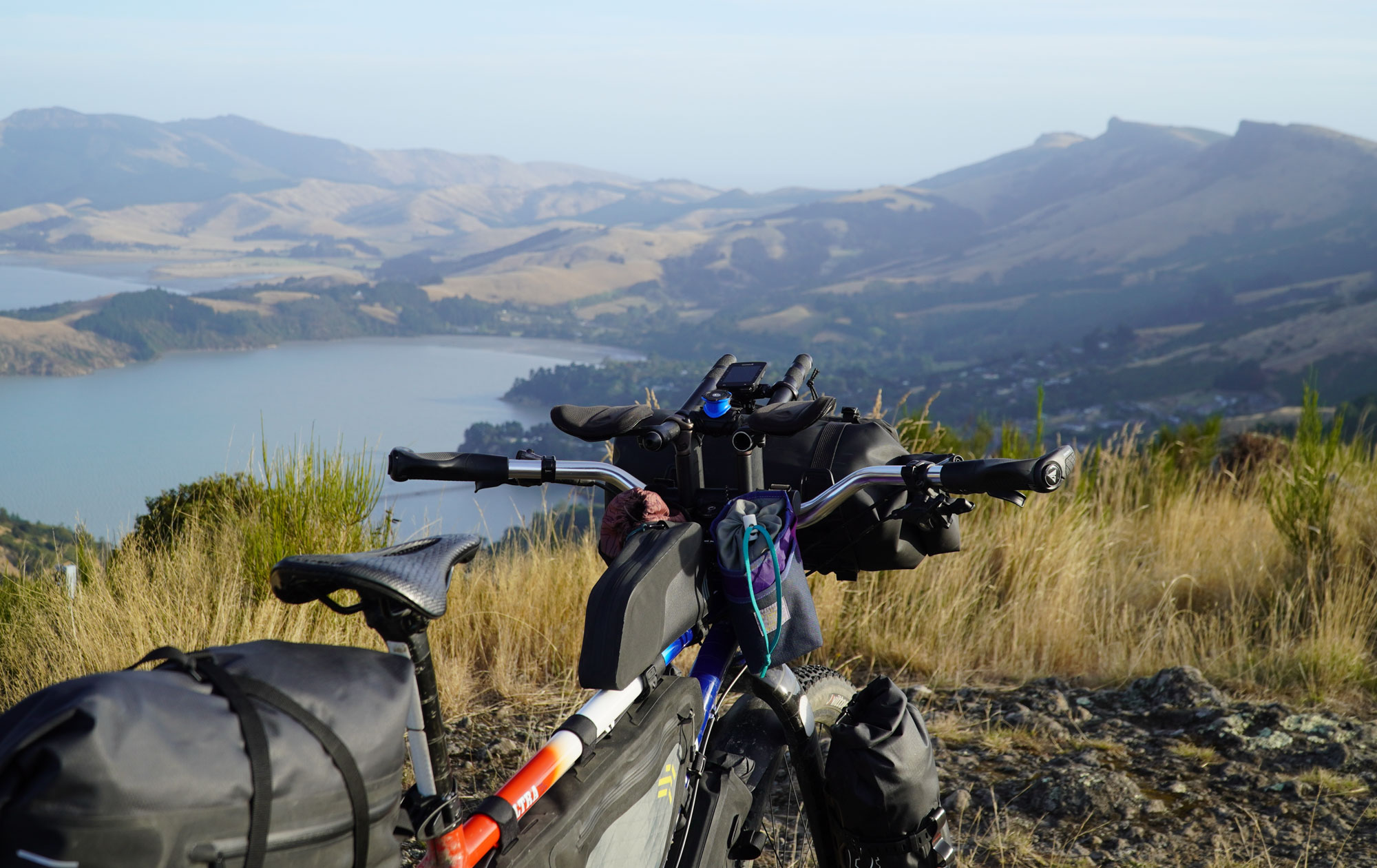 Looking out over a landscape of hills and lakes above a fully loaded Ritchey bikepacking rig, with bags on almost every surface and aero bars peeking above the handlebar bag.