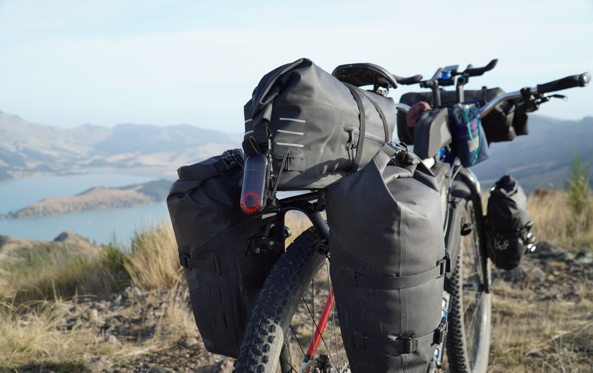 A look at the back end, with three black drybag style bags on the sturdy Tailfin rear rack: two pannier bags and a seat bag. A rear radar/blinkie light sits at the very back.