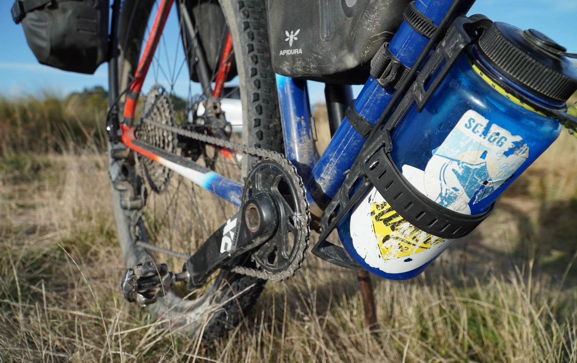A Topeak Versacage and strap holds a battered one-liter Nalgene water bottle under the downtube. The bottle has several faded and illegible stickers on it.