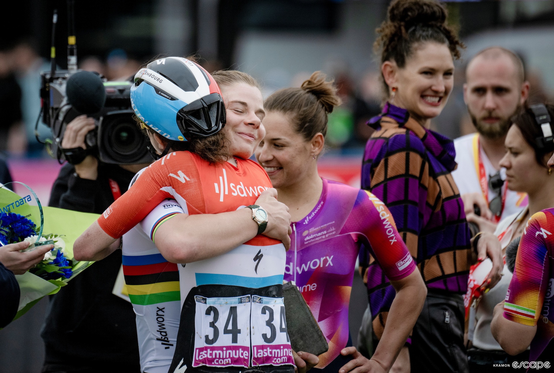 Two teammates of a cycling team hug in a crowd of people. 