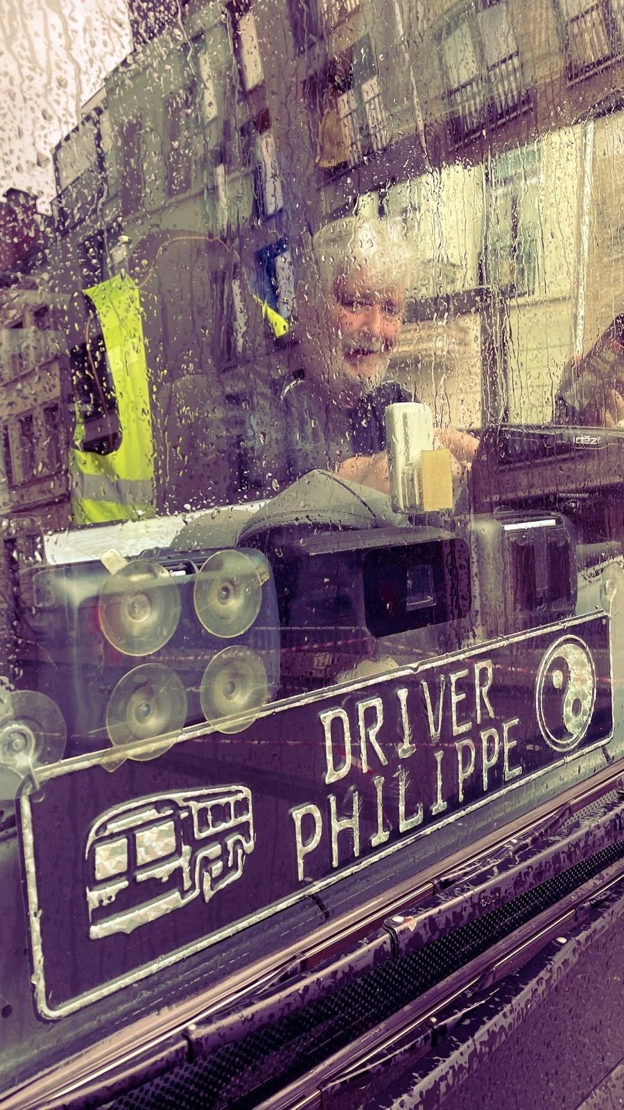 A bus driver, seen through a rain-soaked windscreen