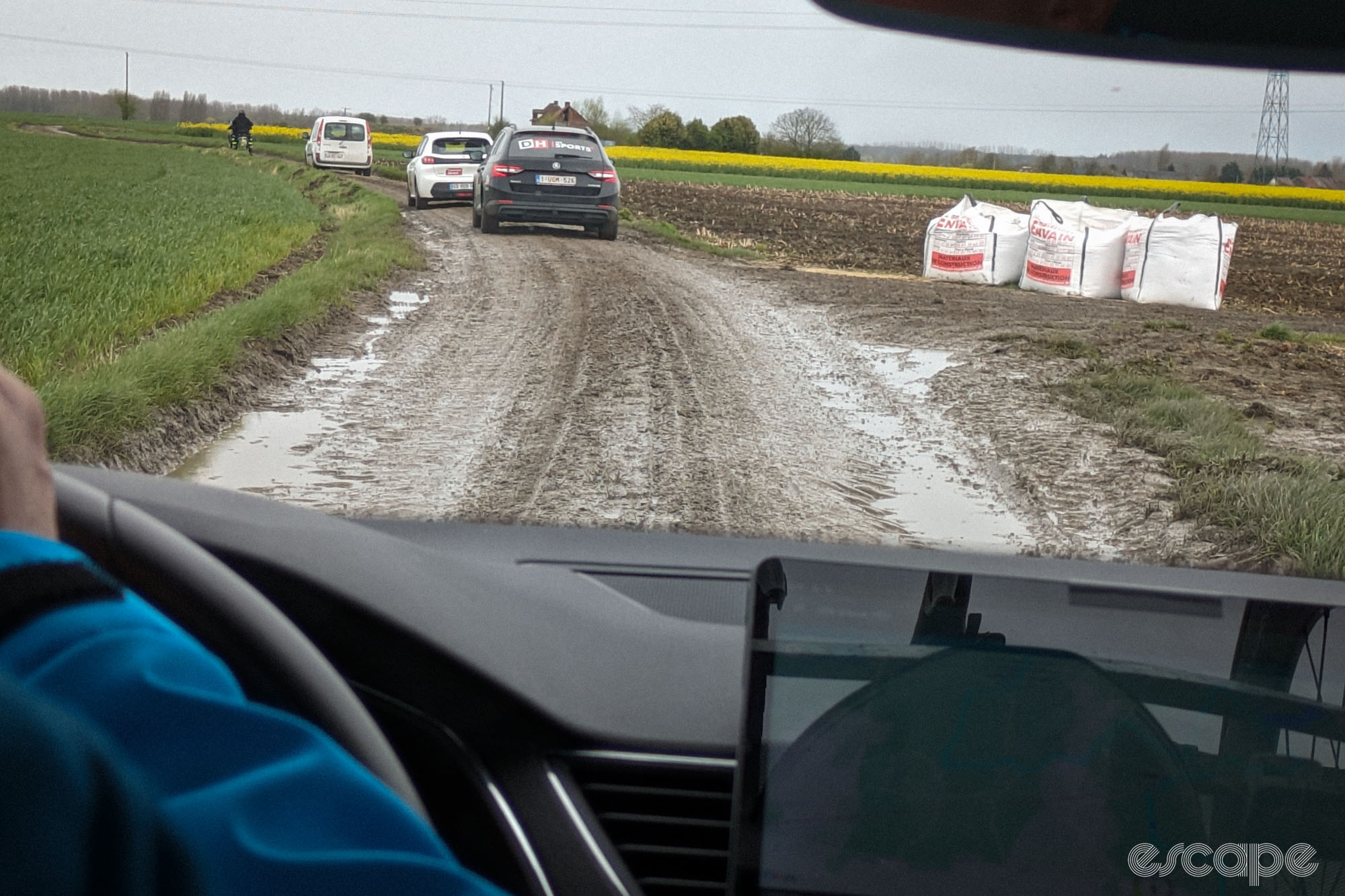 A convoy of cars drives down a cobbled track. The mud is thick on the cobbles and it's not possible to make out the stones.