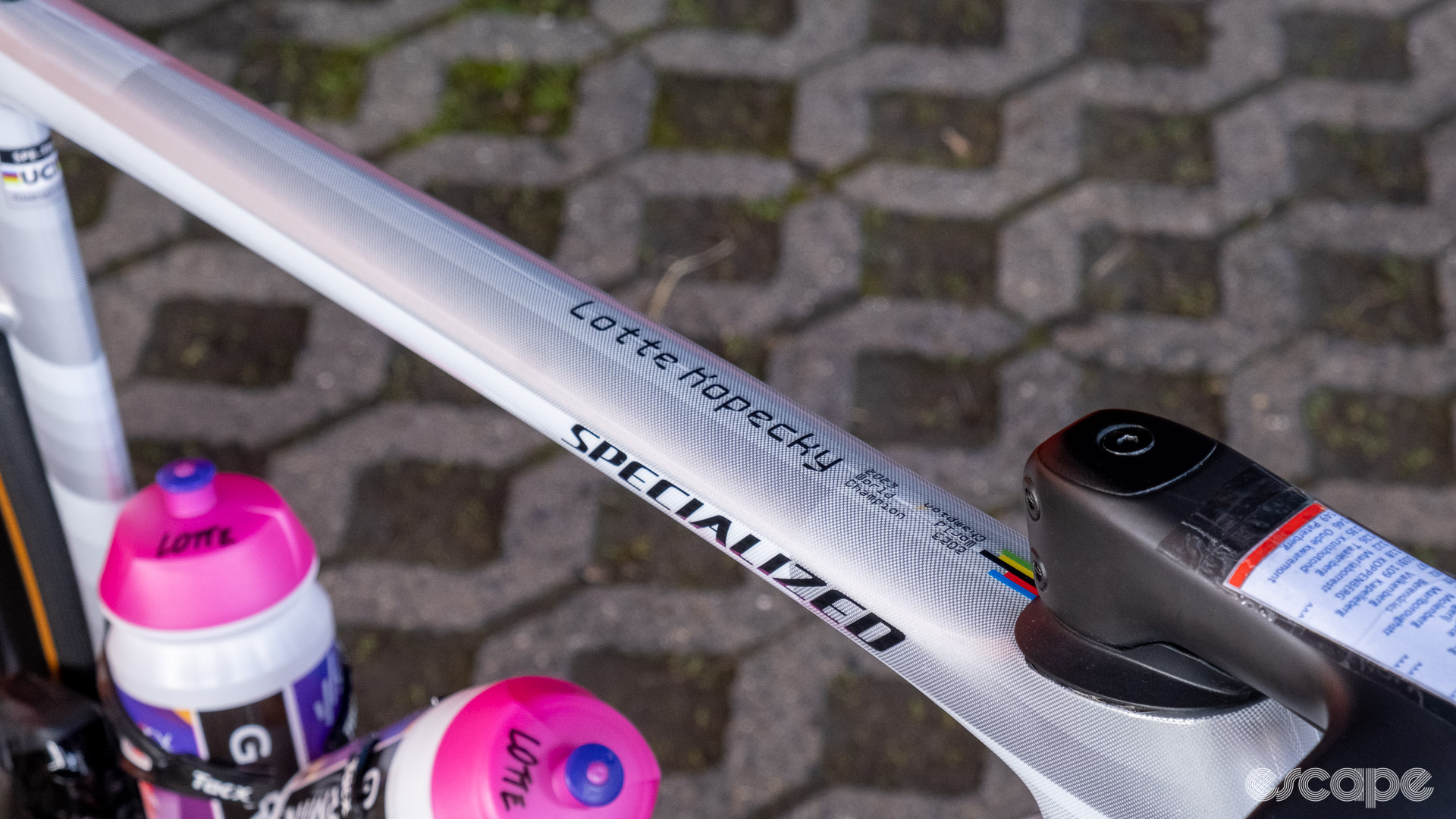 The image shows the top tube of Lotte Kopecky's bike which has her name in large text and th words "2023 World Chmapion" written along side a small rainbow bands decal.