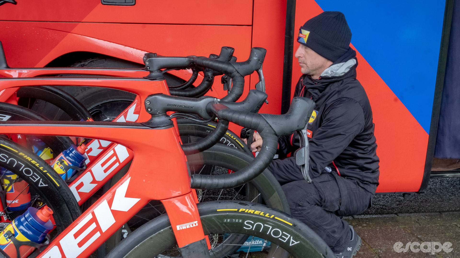 The image shows a Lidl-Trek mechanic and two Trek Madone bikes. The mechanic is checking tyre pressure on one bike.