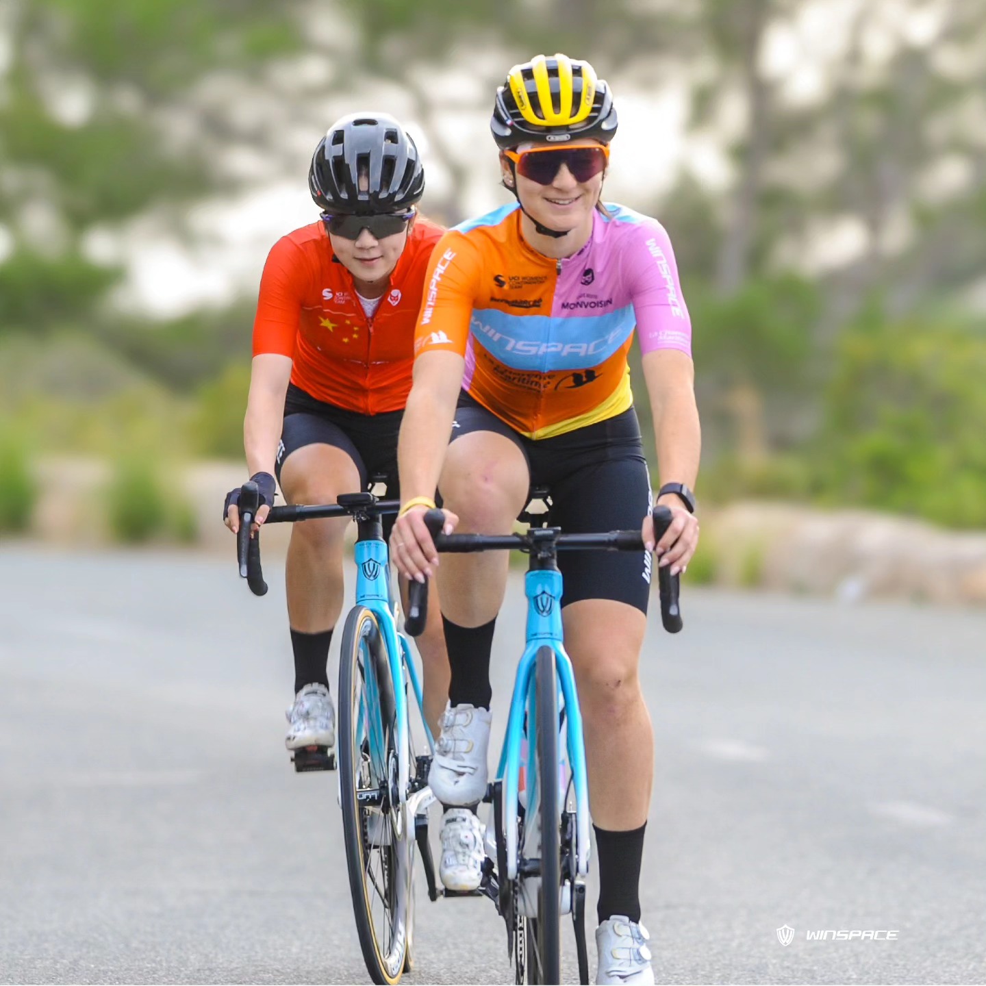 Luyao Zeng rides with a Winspace teammate while training. She has the bright red jersey of Chinese national champion, with the yellow stars of its flag.