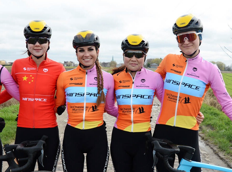 A team of female cyclists stands side by side with their bikes 