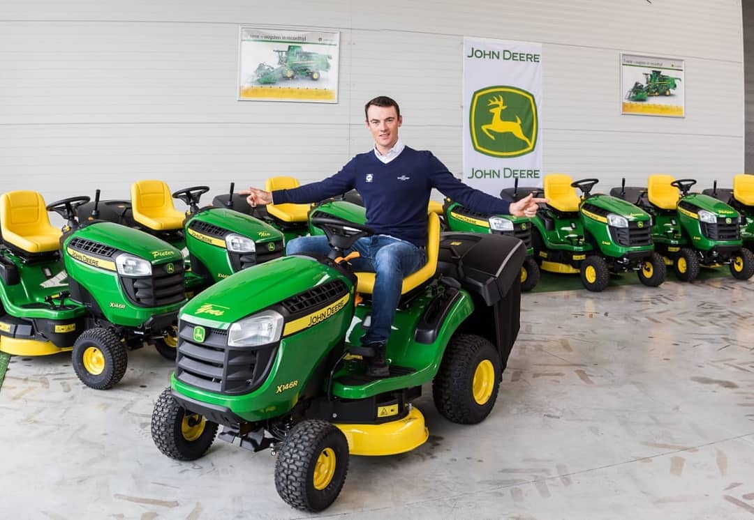 Yves Lampaert sits on a John Deere riding mower in front of a line of them at a local dealership.