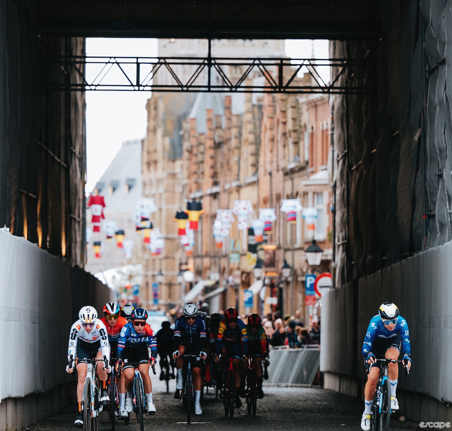 Emma Norsgaard attacks late in Gent-Wevelgem. She rides alone under a large scaffolding on a bridge. The other riders aren't looking at her yet.