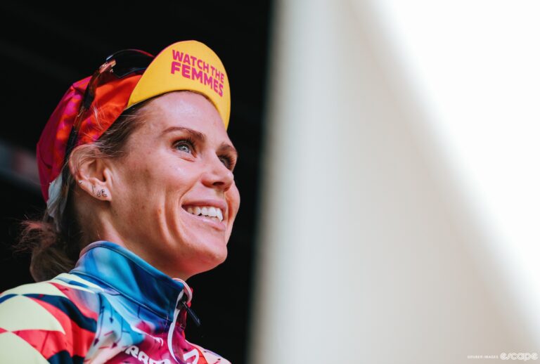 A woman in cycling clothing smiles and looks into the distance