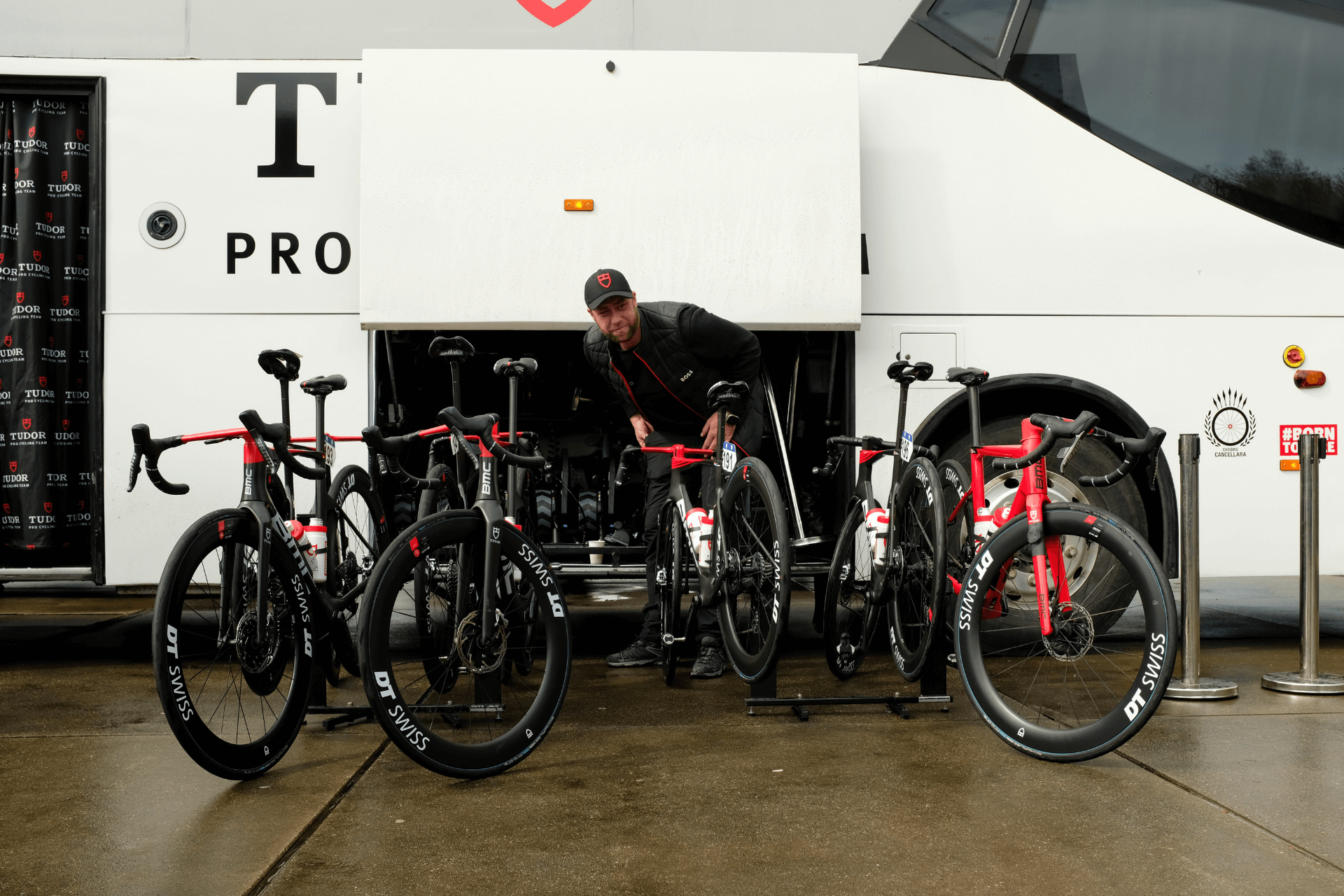 A row of high end road bikes being prepped by a mechanic in front of a team bus