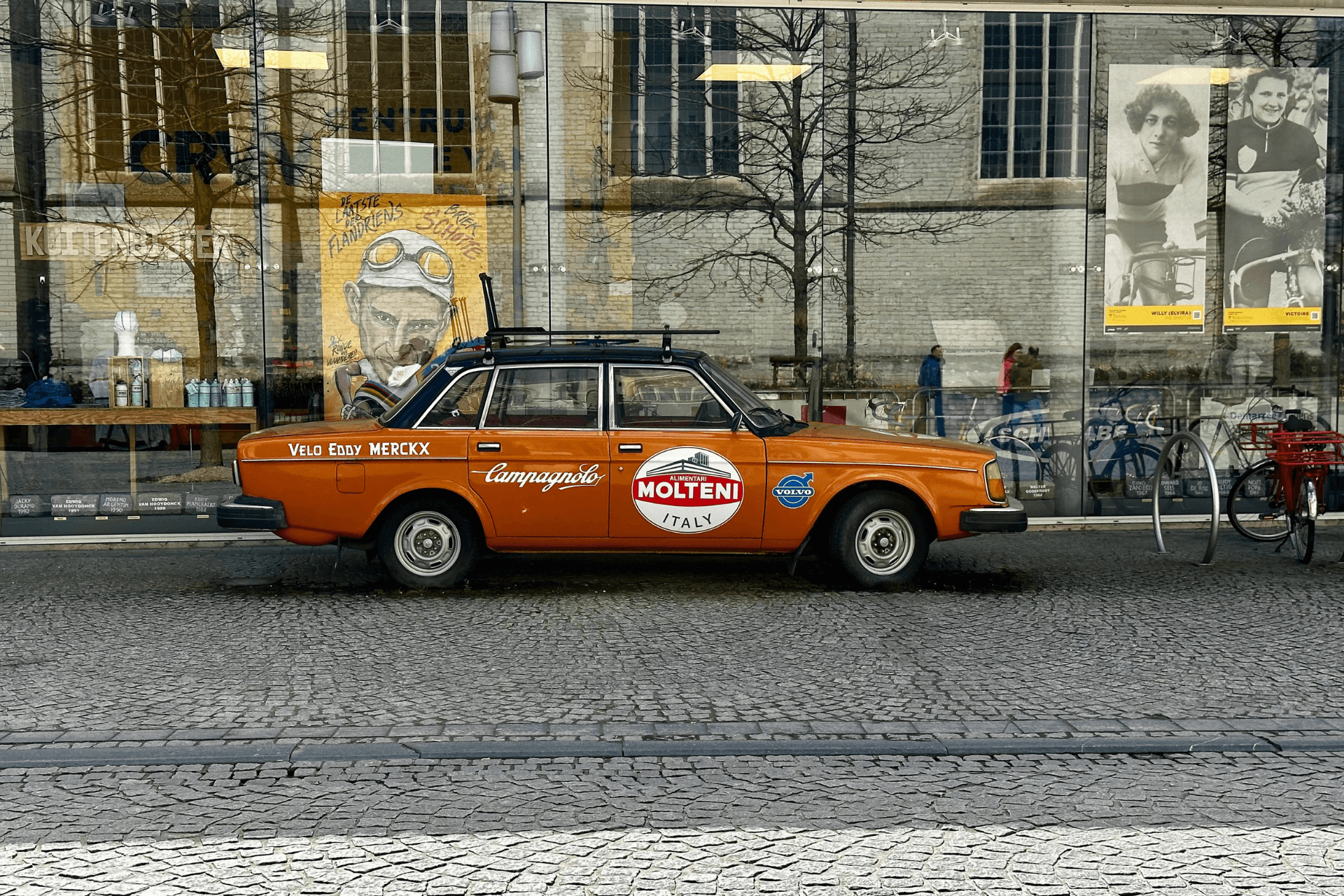 A 70s era Volvo sporting Molteni and Campagnolo decals parked out front of a building with large glass frontage