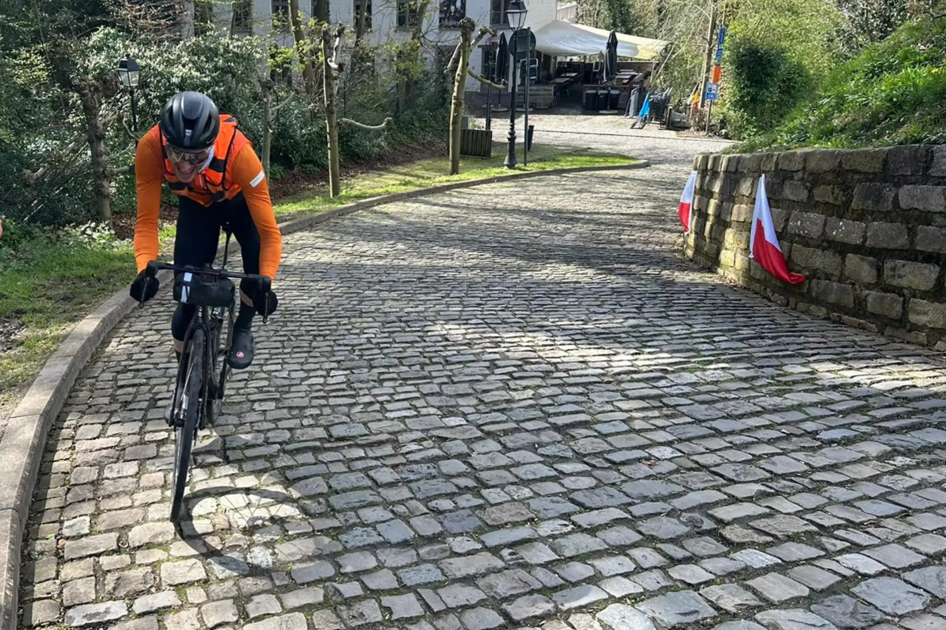 A road cyclist in bright orange gear is riding up a cobbled road